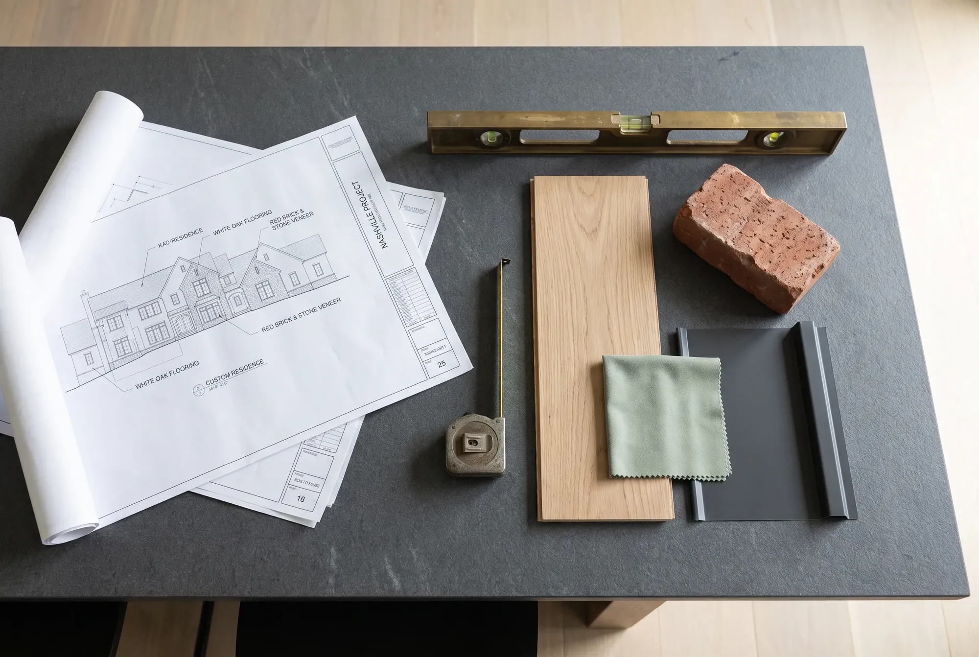 Architectural plans for a custom home laid out with a level, a tape measure and white oak and brick samples