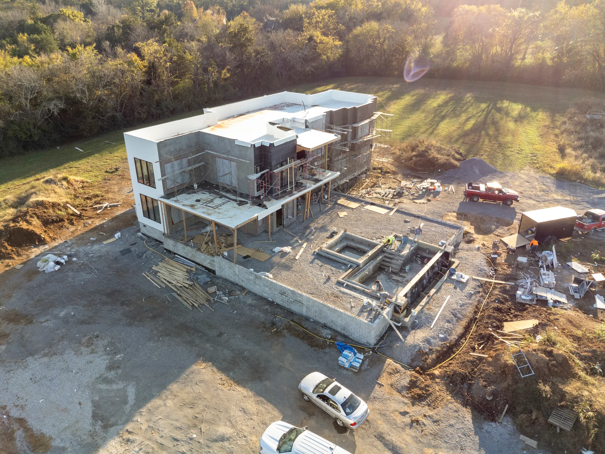 Aerial view of a large white multi-unit building under construction with scaffolding, block foundation walls and concrete pool shells being formed nearby