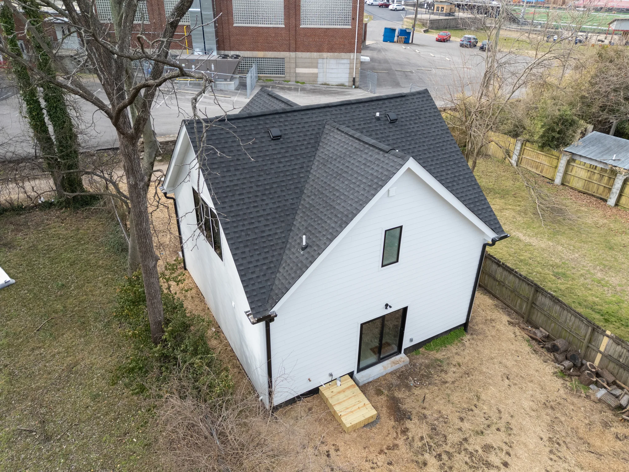 Aerial view of a newly built white lap-sided house with dark shingled gable roofs, black-framed windows and a temporary wood step at the rear door