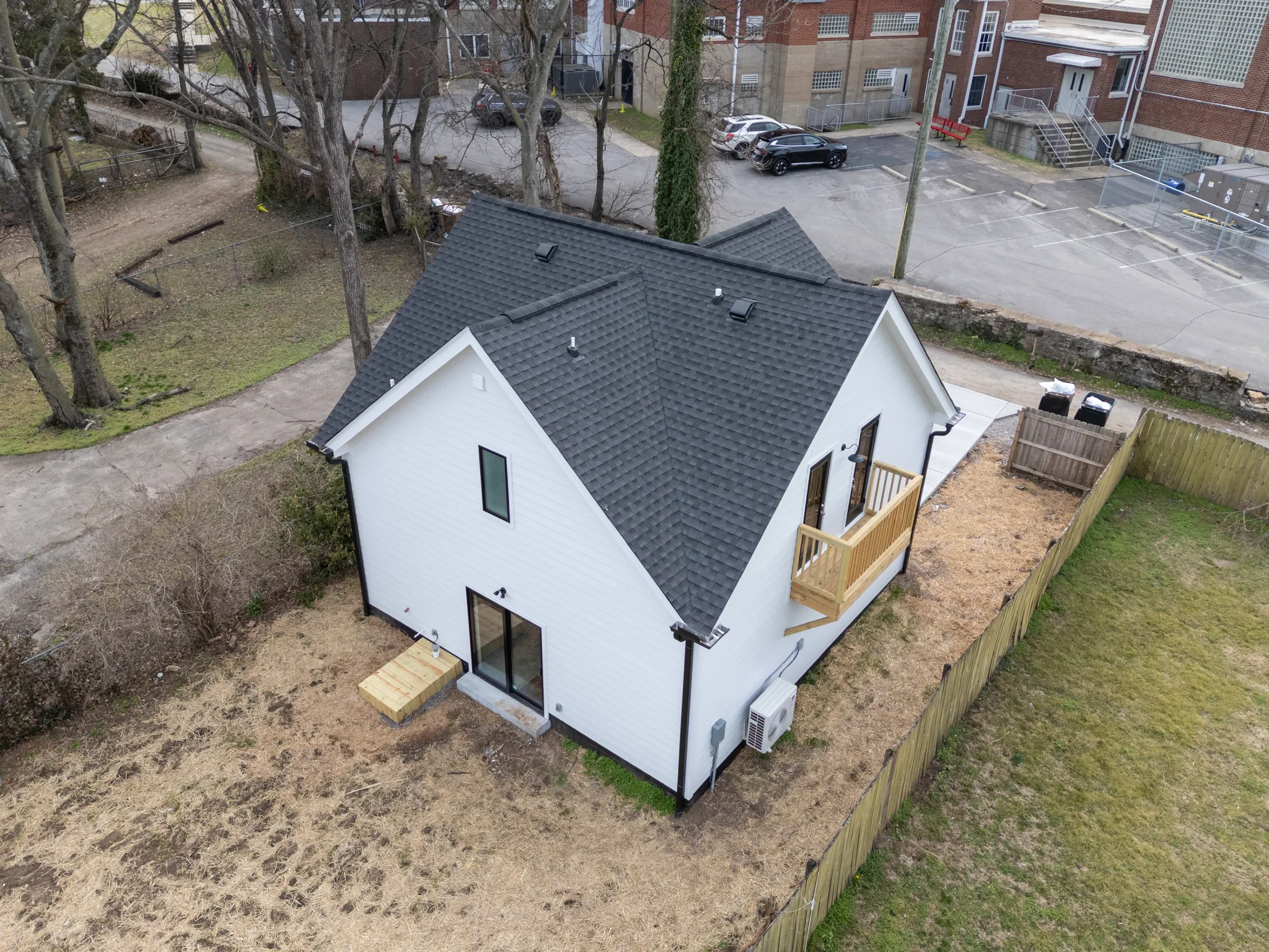 Aerial view of a white lap-sided home with steep dark shingle gable roof, small wood balcony, temporary landings and a wood privacy fence
