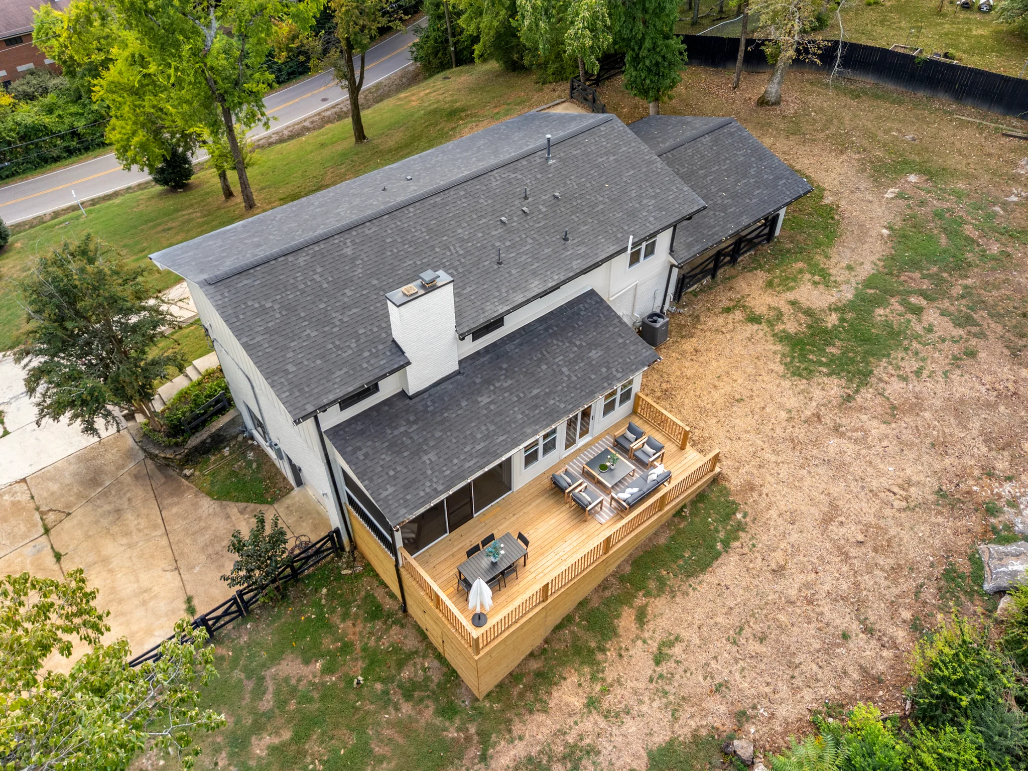 Aerial view of a painted white house with gray shingle roof and a large new wood deck holding patio furniture along the back