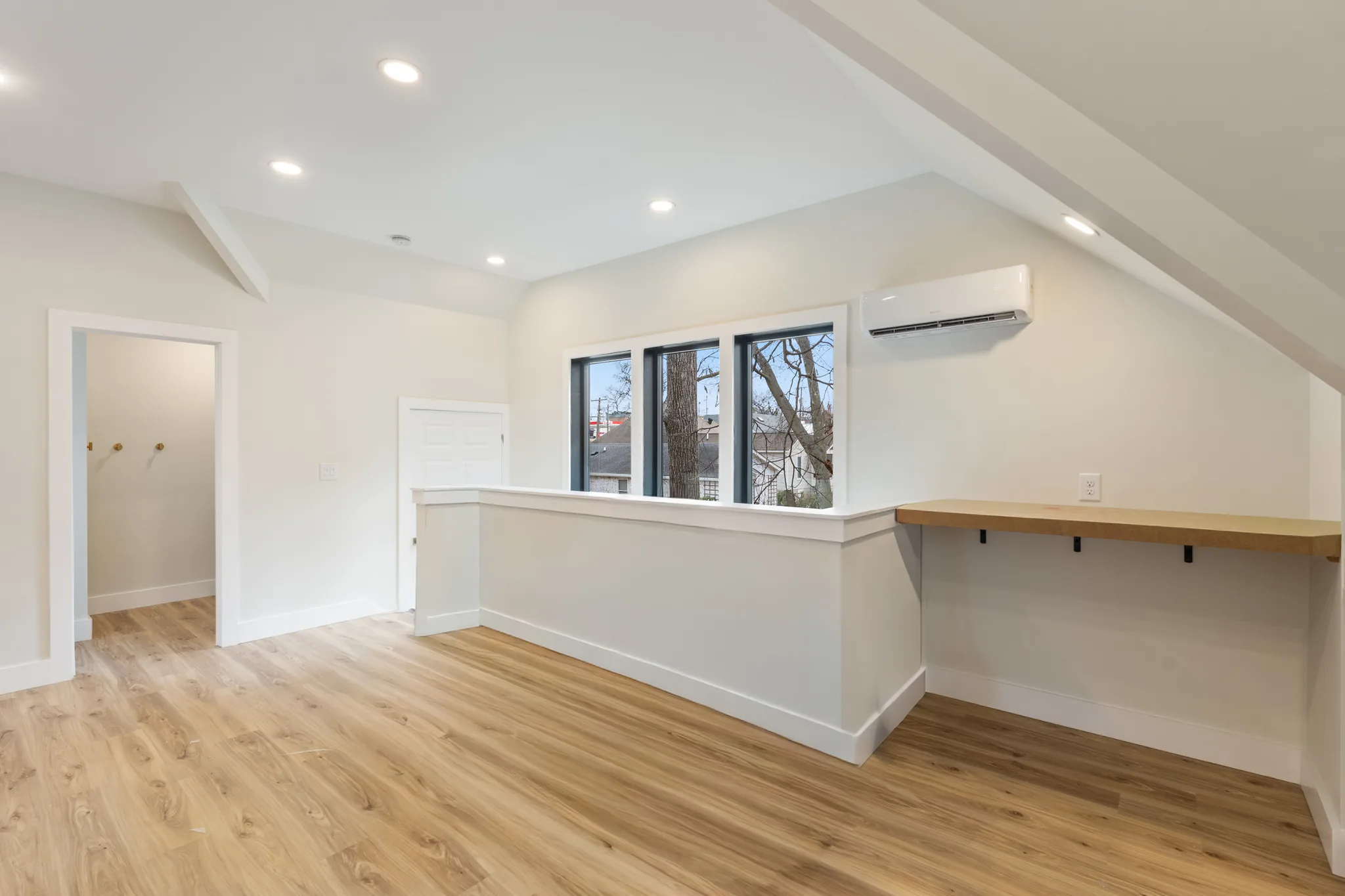 Finished attic bonus room with white sloped ceilings, half-wall partition, wood-look plank flooring, wall-mounted mini split and a wood bar ledge