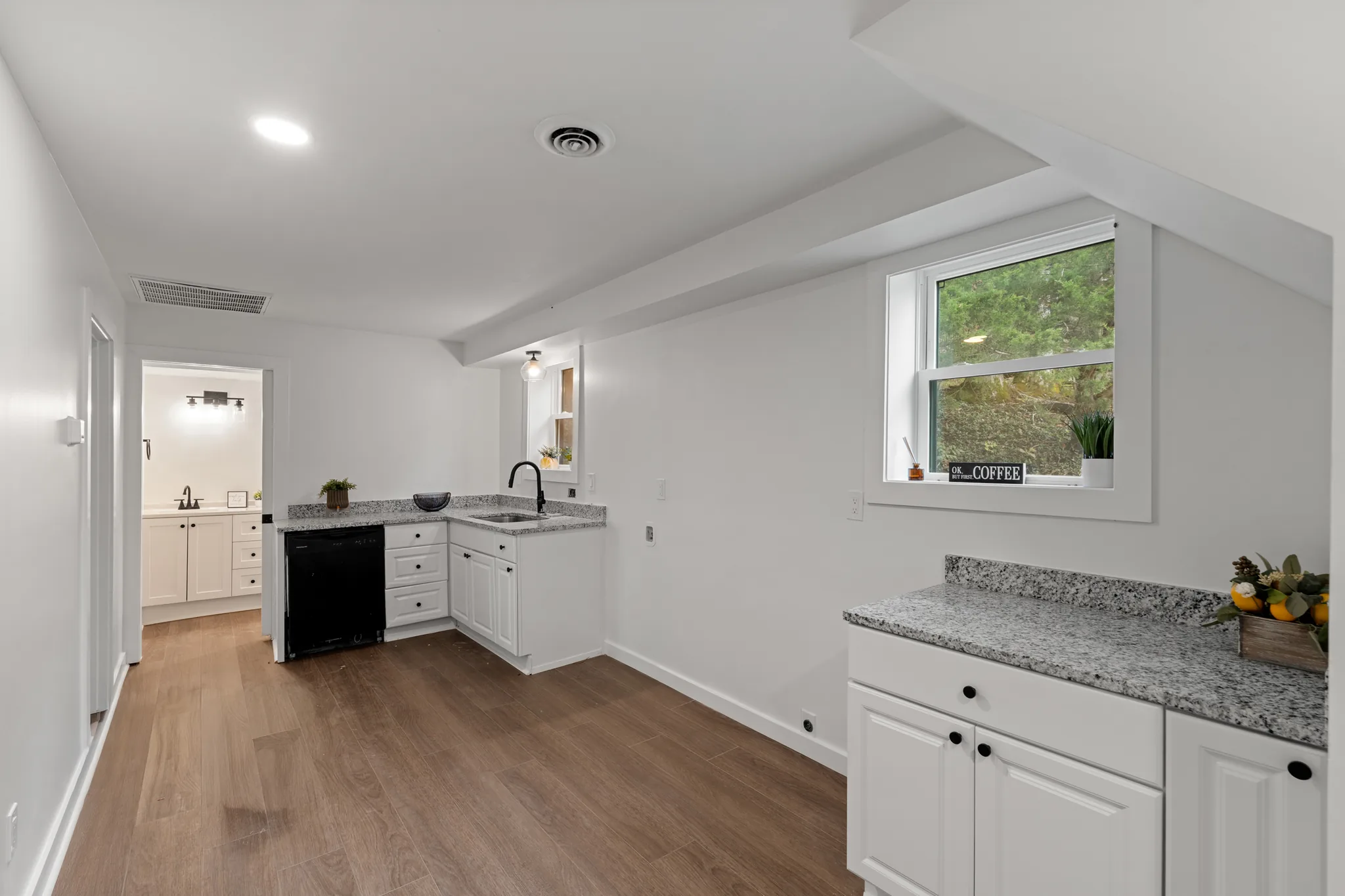 Basement wet bar with white shaker cabinets, speckled granite counters, black undercounter refrigerator and a second granite counter under a sloped ceiling