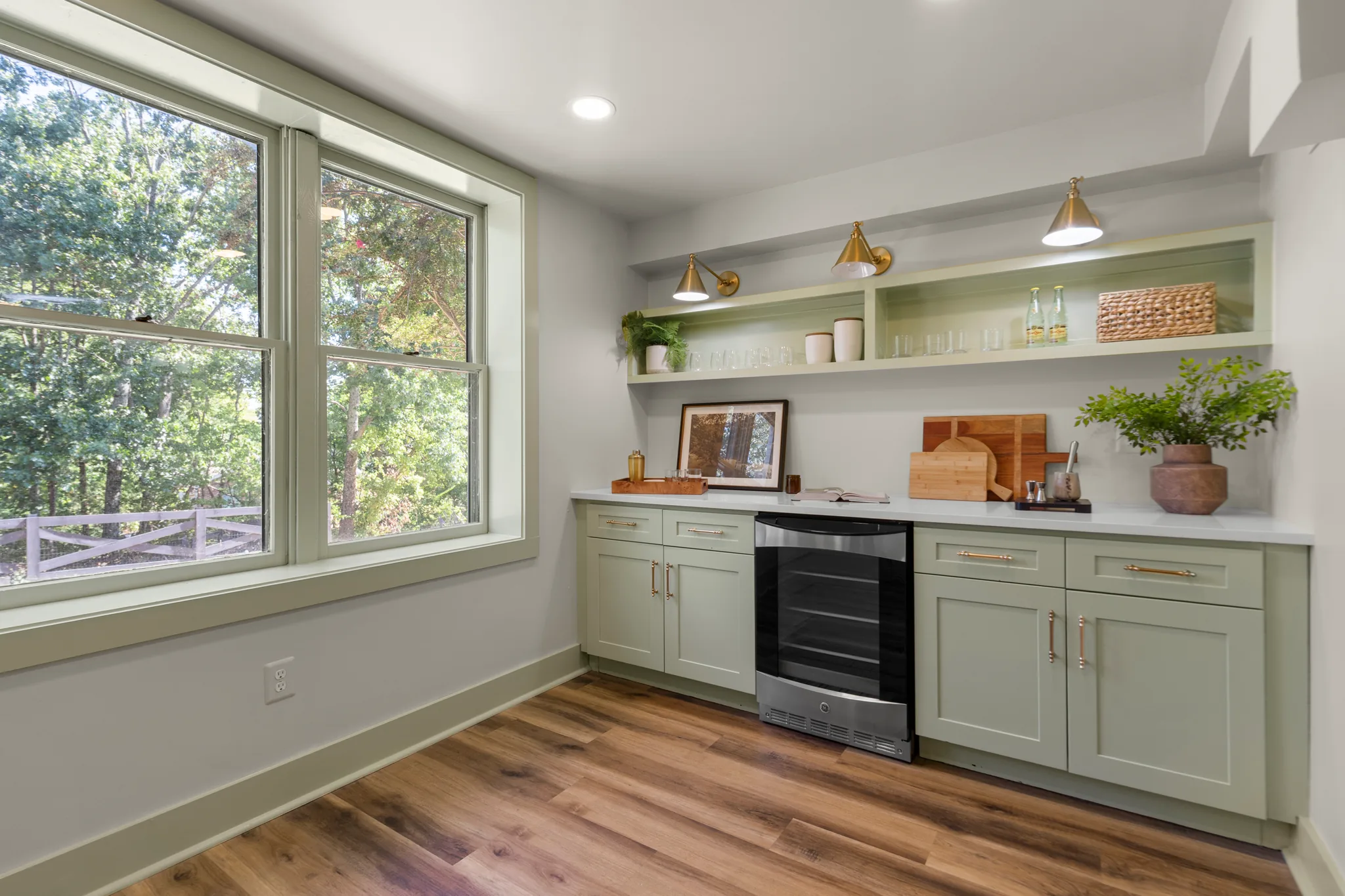 Beverage bar with sage green shaker cabinets, white quartz counter, open shelving, brass sconces, stainless wine fridge and wood floors