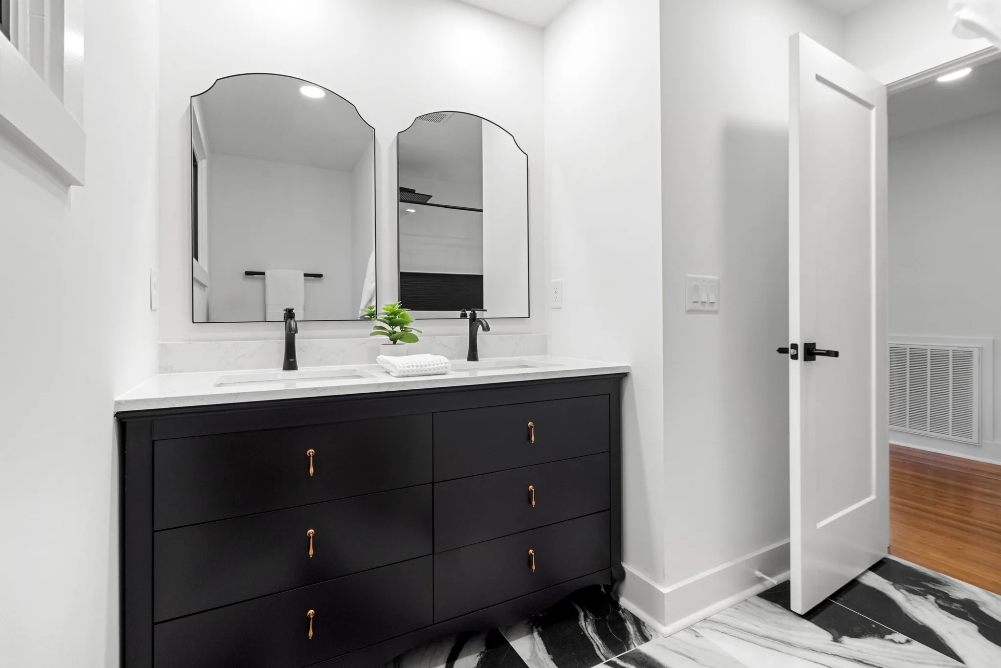 Bathroom with a black double vanity, white quartz counter, two arched mirrors, black faucets, brass pulls and black and white marble tile floor