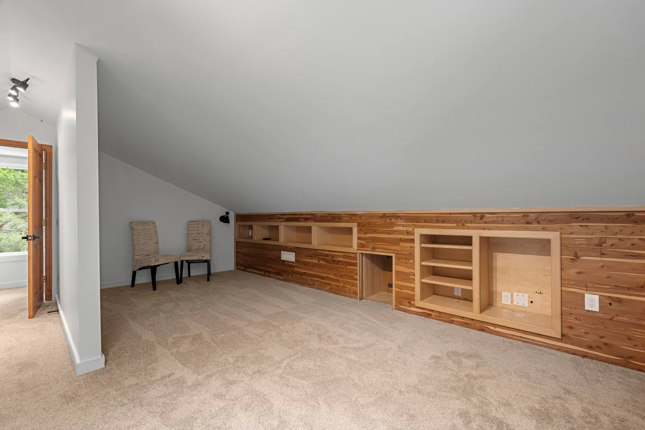 Finished bonus room with sloped ceiling, gray walls, carpeted floor and cedar plank knee wall holding open built-in shelving and niches
