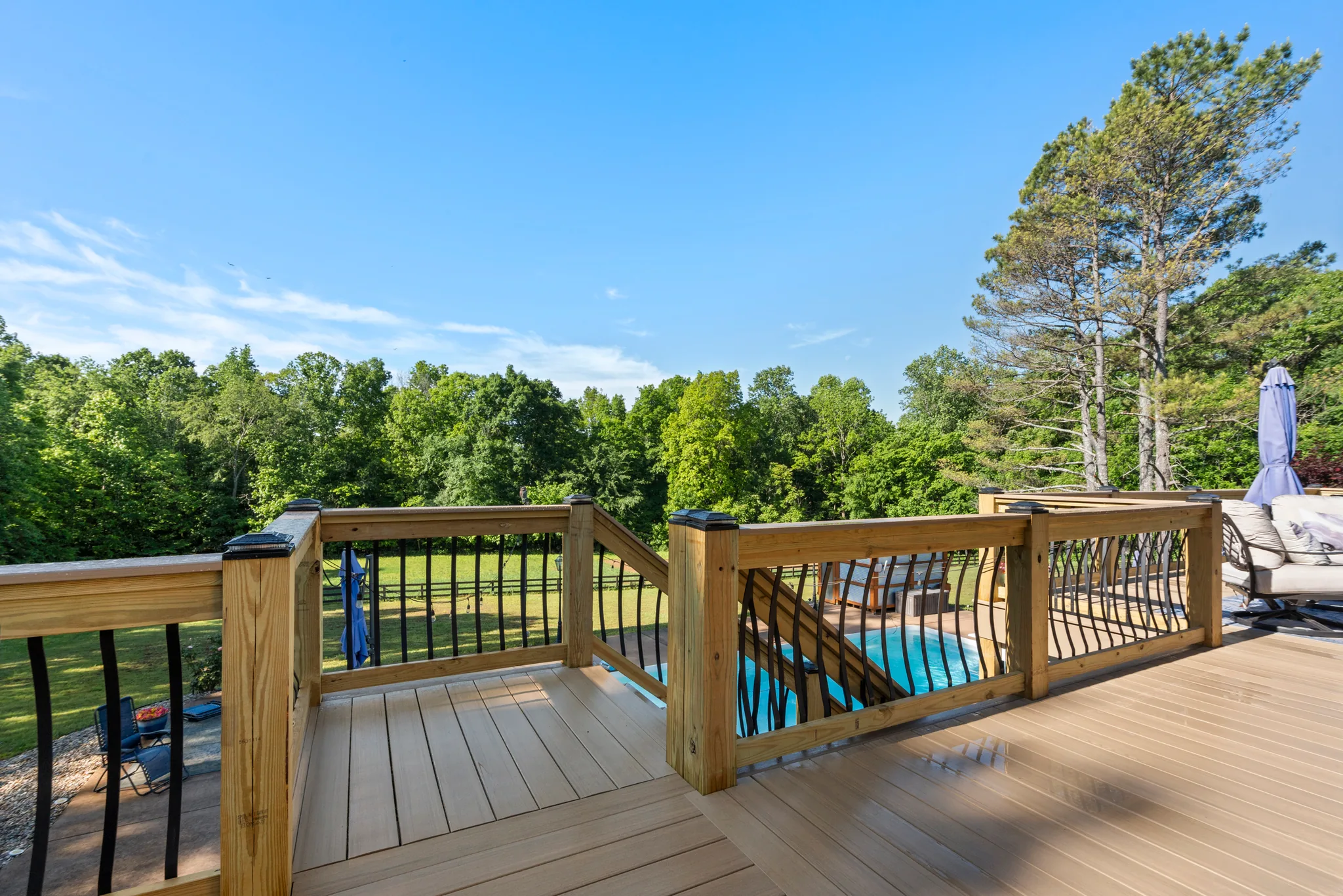 Composite deck corner with pressure-treated railing posts, black balusters and post cap lights overlooking a fenced lawn and a pool below
