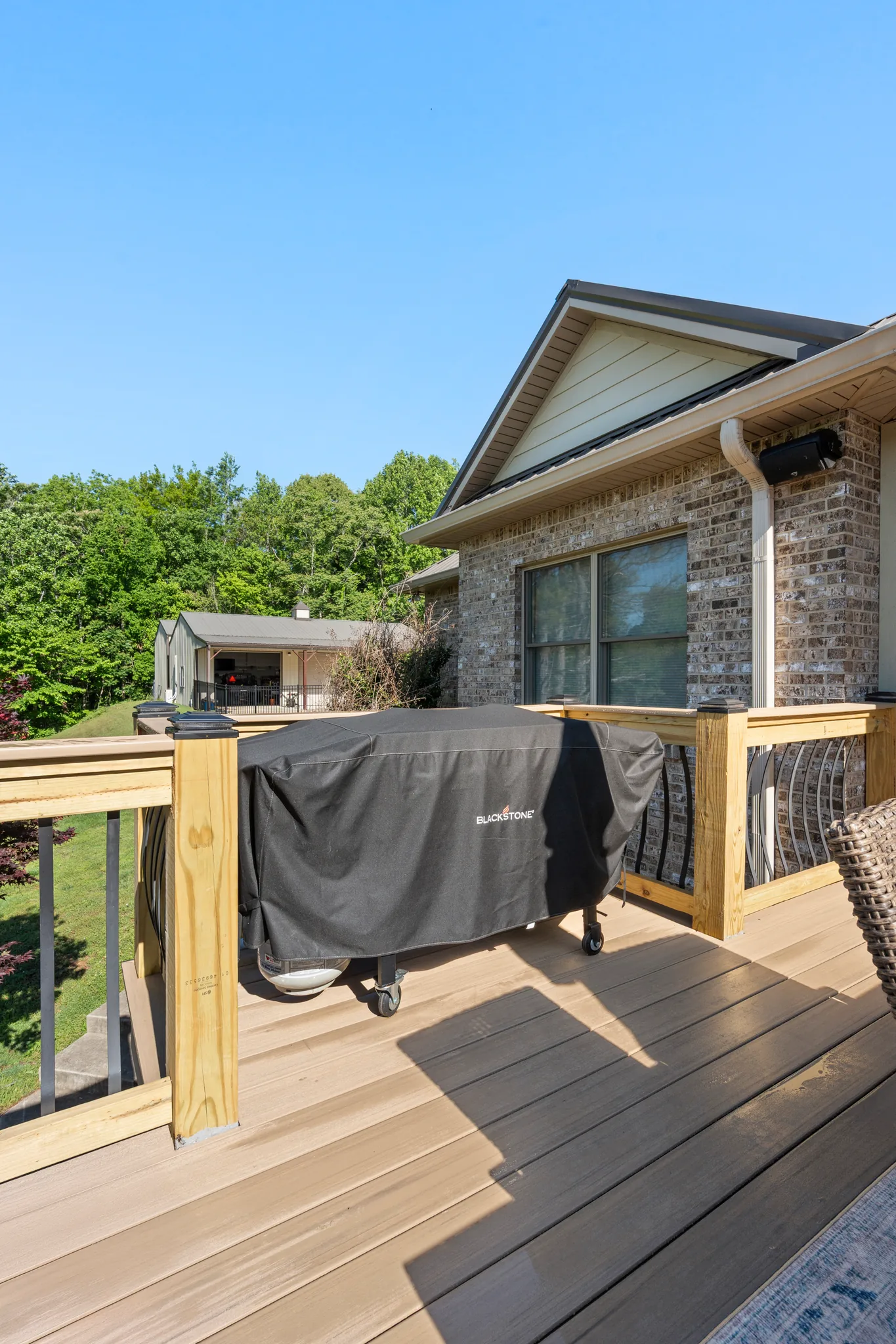 Composite deck with a covered griddle beside wood post railing and decorative metal balusters, next to a brick home with gabled roof