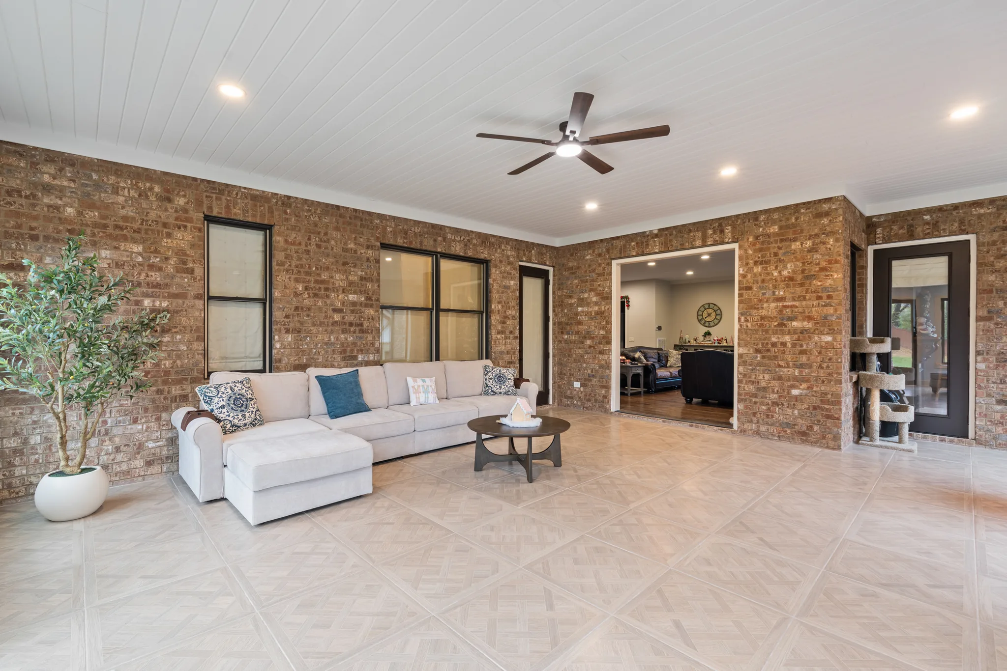 Large covered porch with brick walls, white plank ceiling, recessed lights, a dark ceiling fan and cream tile floor with sectional seating