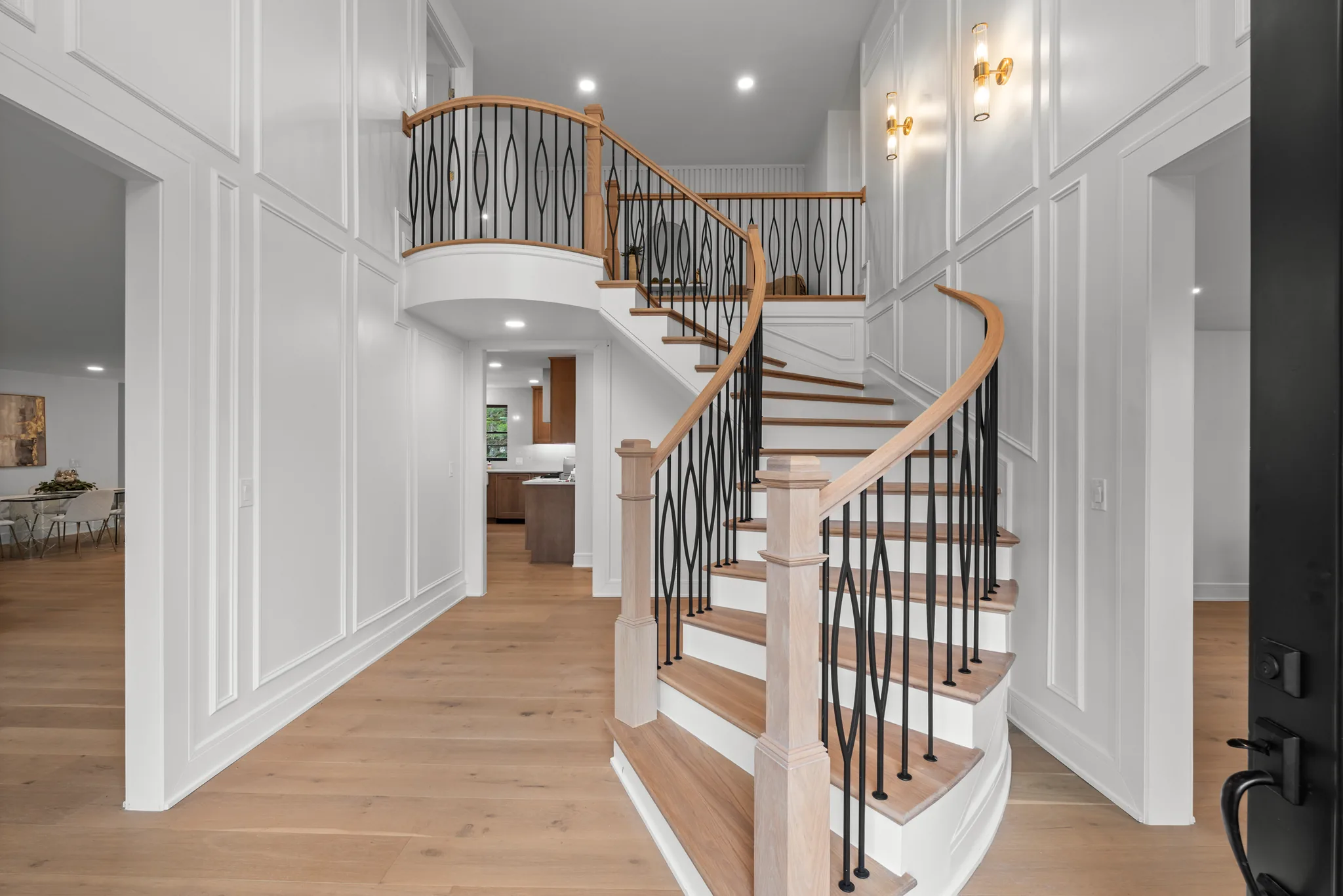 Curved staircase with oak handrail, black iron balusters and white risers in a two-story entry with paneled walls and oak floors