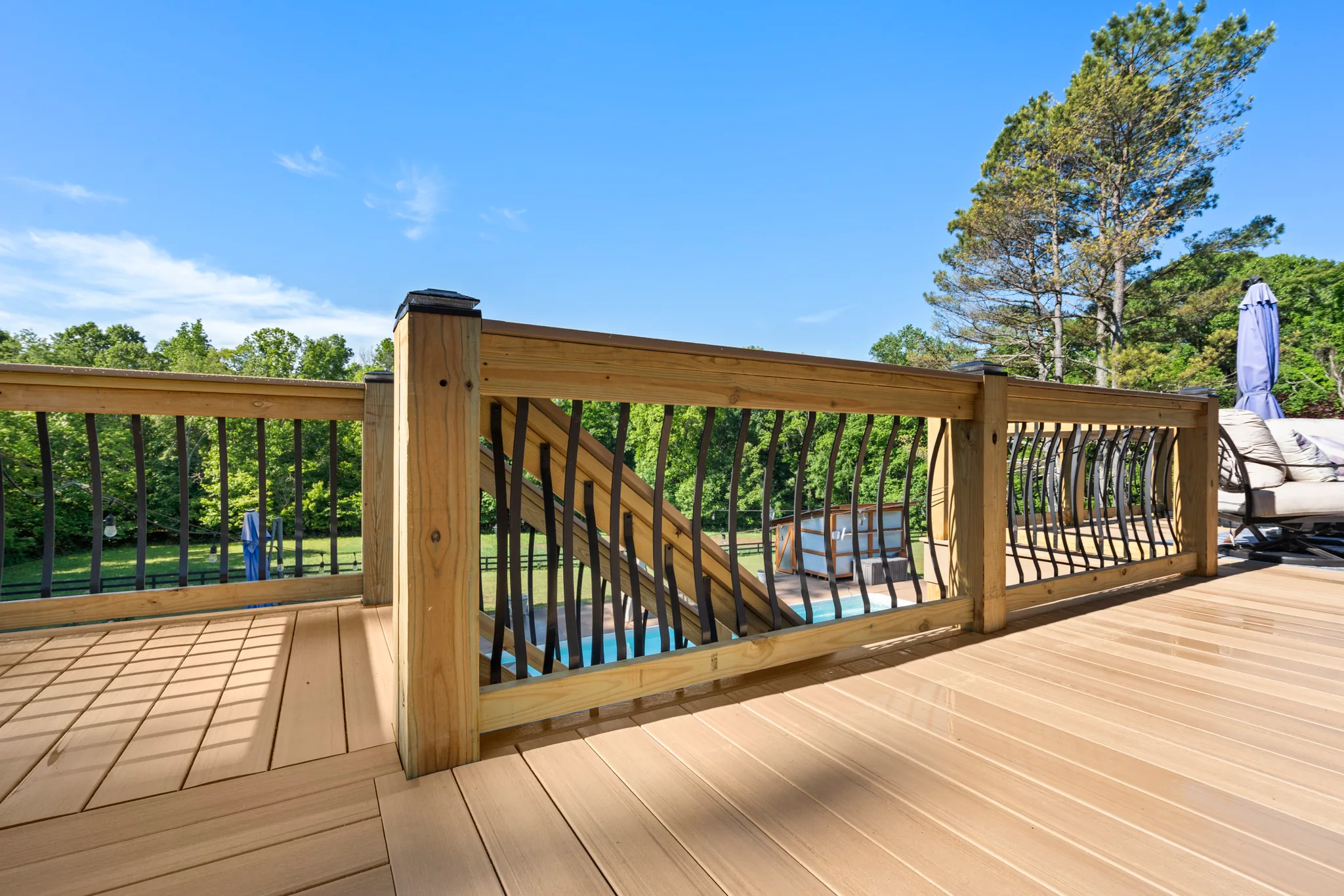 Composite deck with pressure-treated railing and black branch-shaped metal balusters overlooking a pool with a slide and wooded backyard