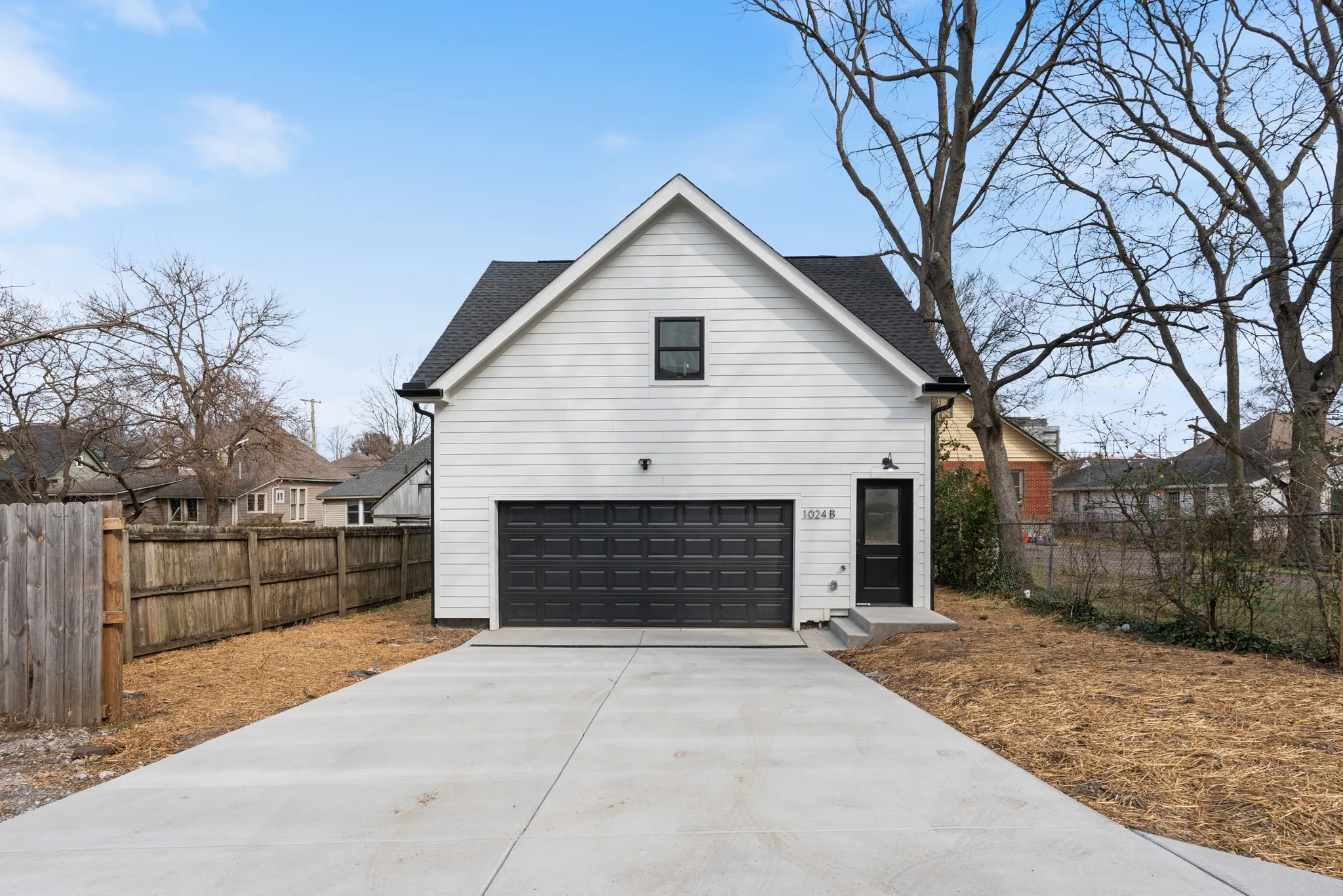 Detached two-story garage with white lap siding, black sectional garage door, black entry door and a wide concrete driveway leading to it
