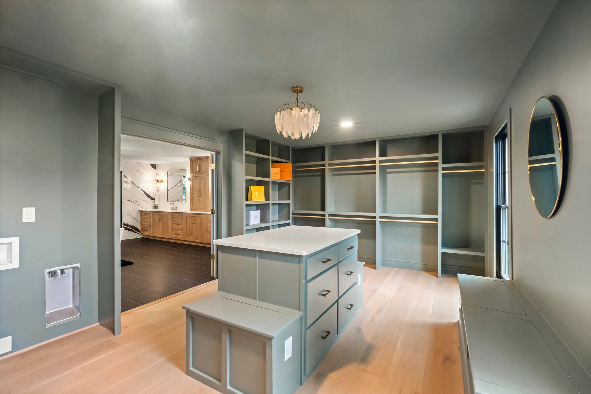 Walk-in dressing room with sage green built-in shelving, hanging rods, a quartz-topped island with drawers and light oak plank flooring