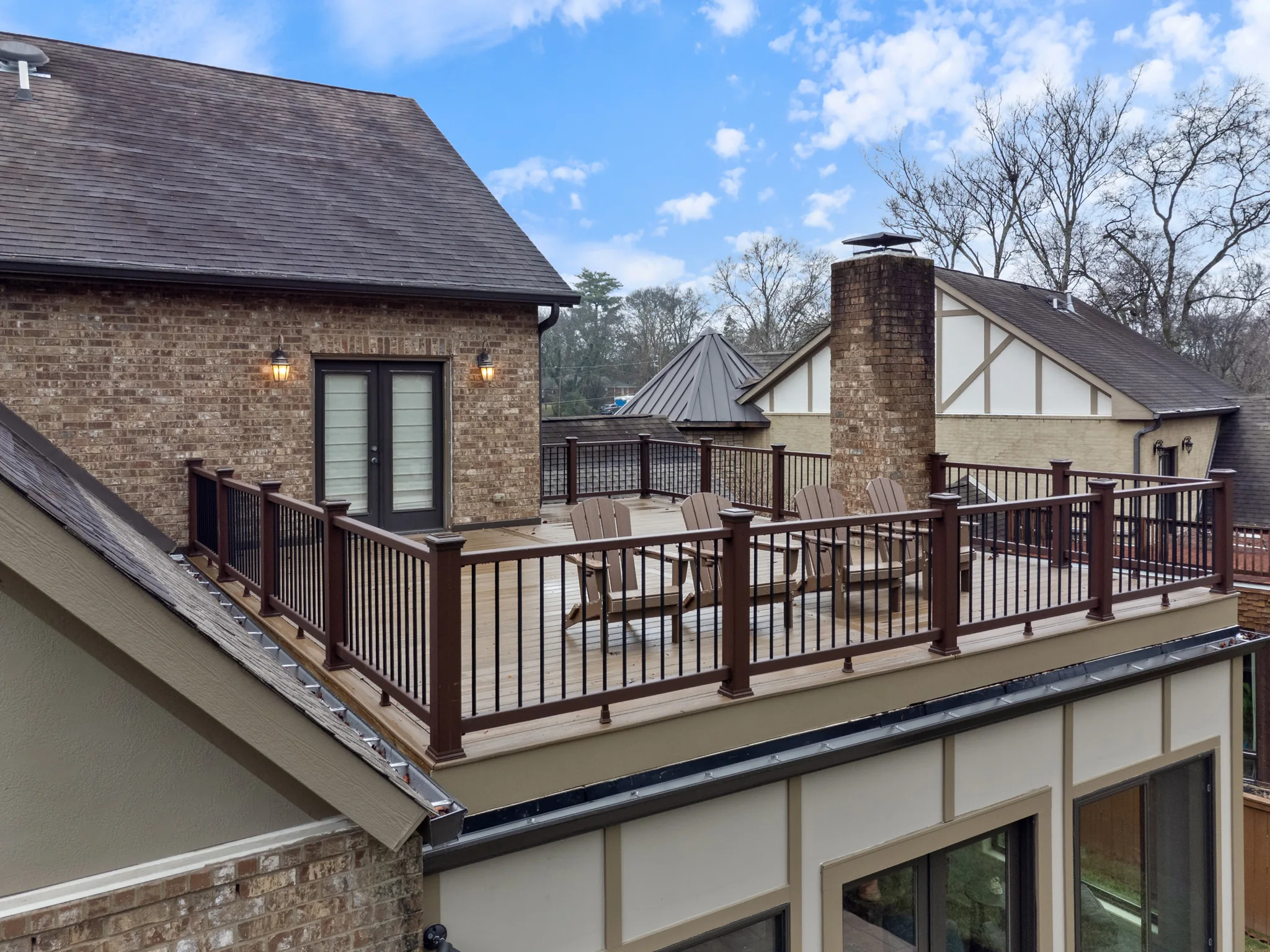 Elevated composite deck with brown railing and black balusters set between a brick gable wall with French doors and a tall brick chimney