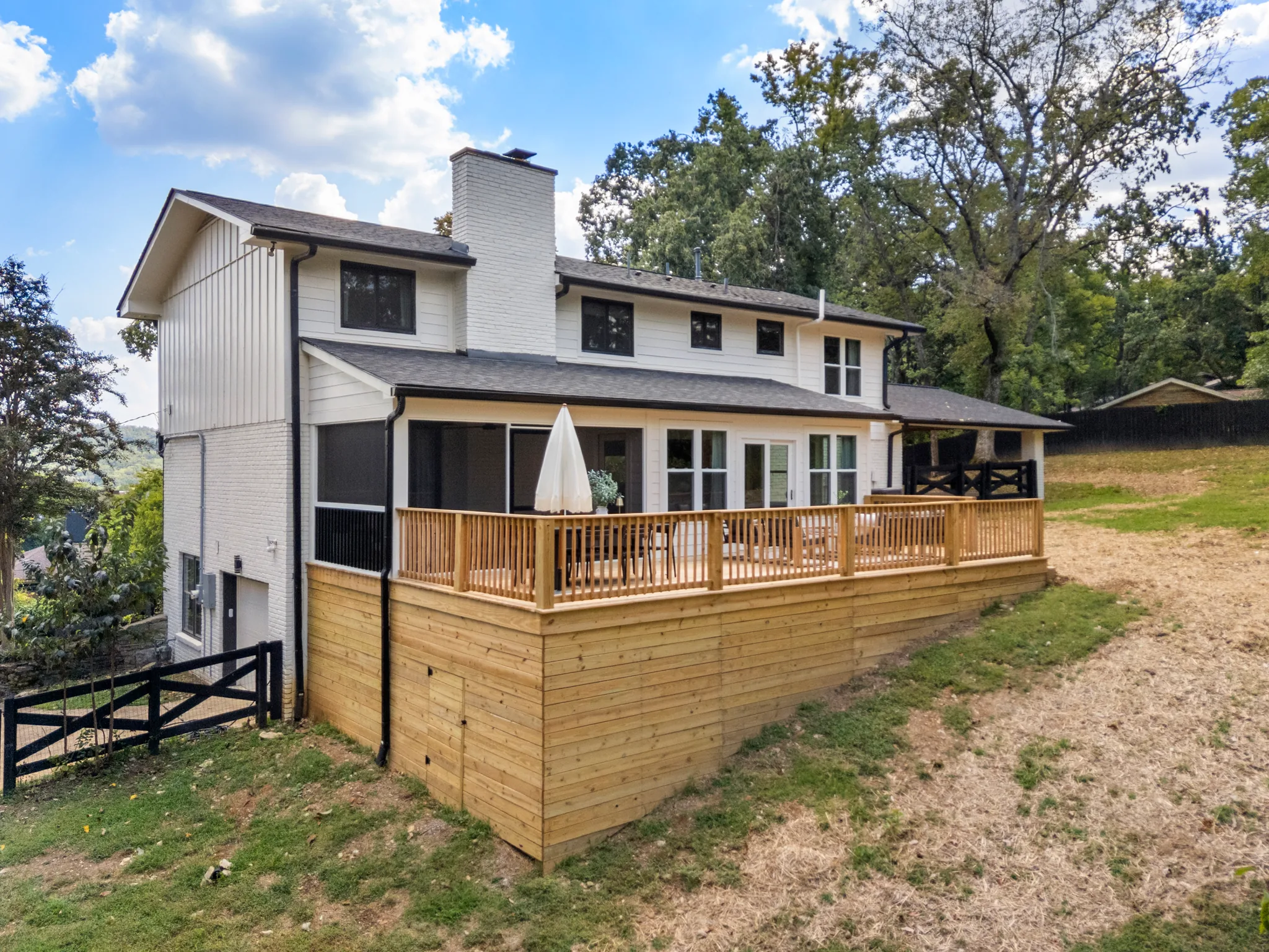 Elevated wood deck with railing and horizontal board skirting spanning the rear of a white two-story house with brick chimney