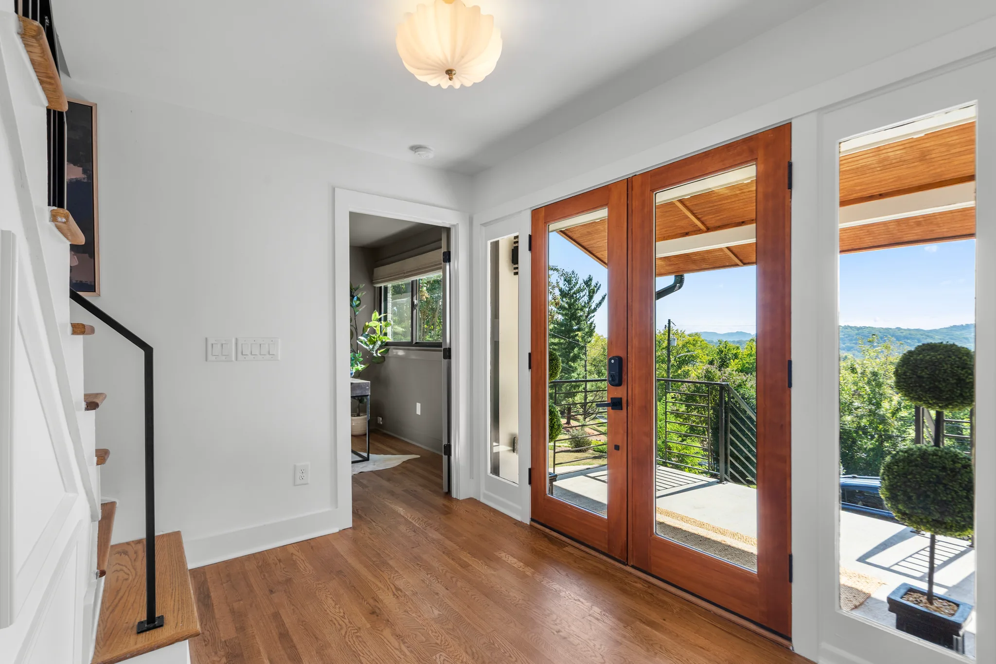 Entry area with stained wood French doors and sidelights opening to a deck with cable railing and hill views beyond
