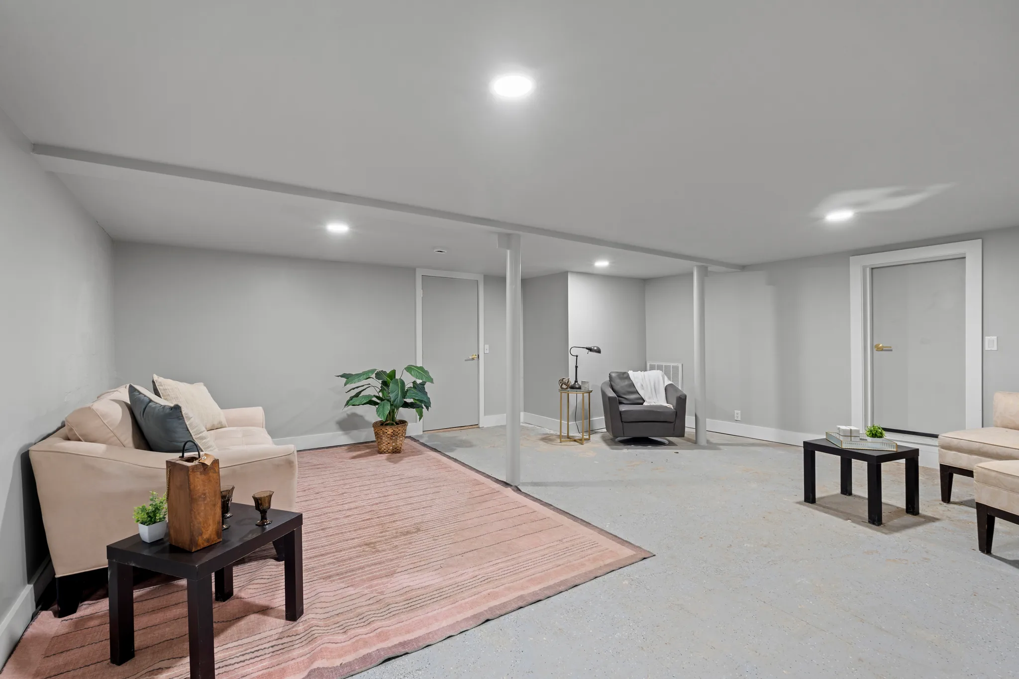 Finished basement living area with gray walls, painted steel support columns, recessed lights, sealed concrete floor, sofa, armchair and area rug