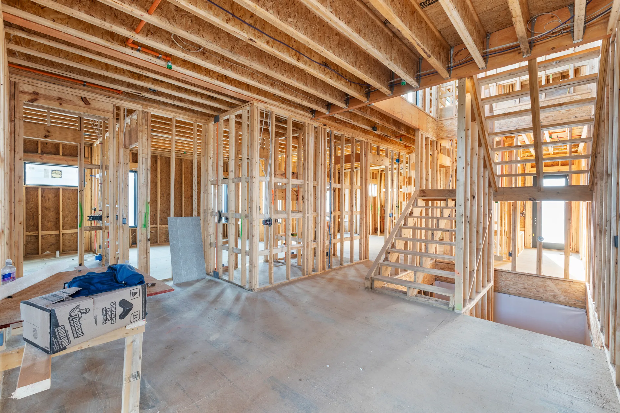 Interior wood framing under construction with open stair stringers, exposed floor joists, rough wiring and a concrete slab floor