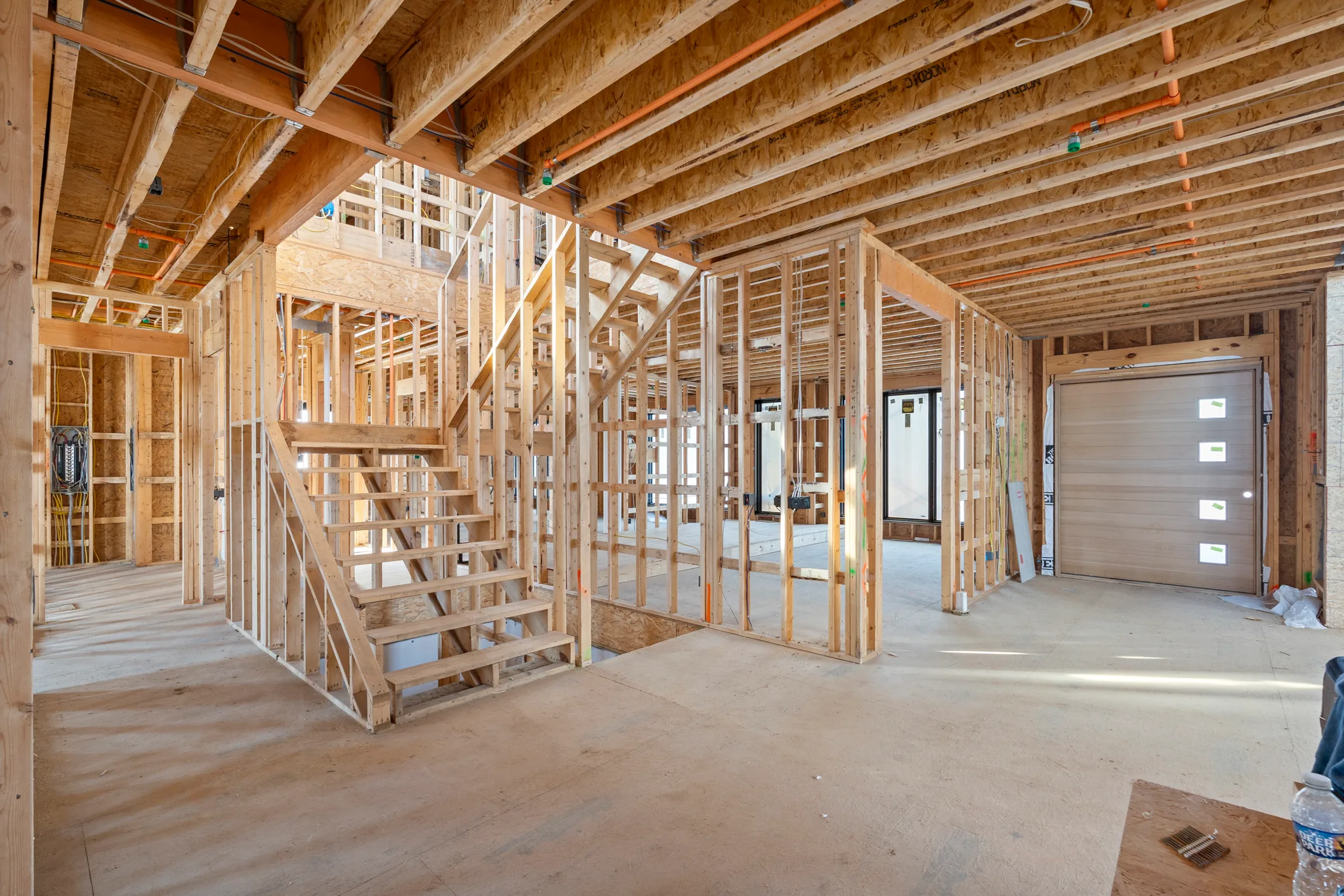 Interior framing under construction on a lower level with wood stud walls, open stair stringers, exposed joists and an installed sectional garage door
