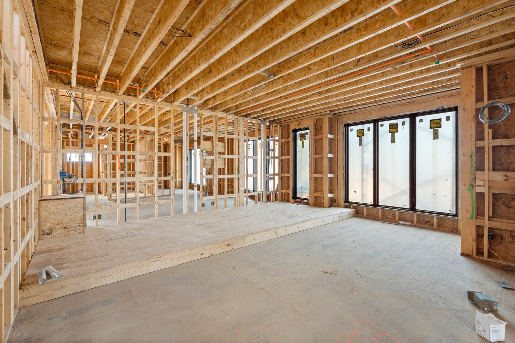 Interior framing under construction with exposed joists, PEX and wiring overhead, a wood step-down, and black sliding glass doors set in the wall