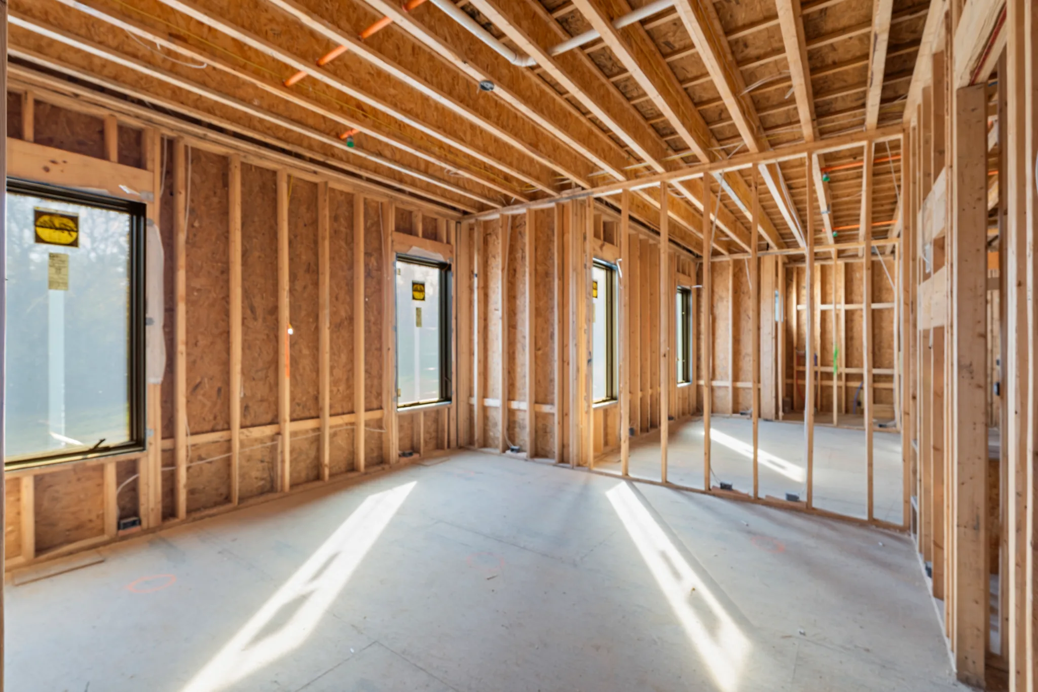 Interior room under construction with exposed wood studs, ceiling joists and newly installed black windows above a bare concrete floor