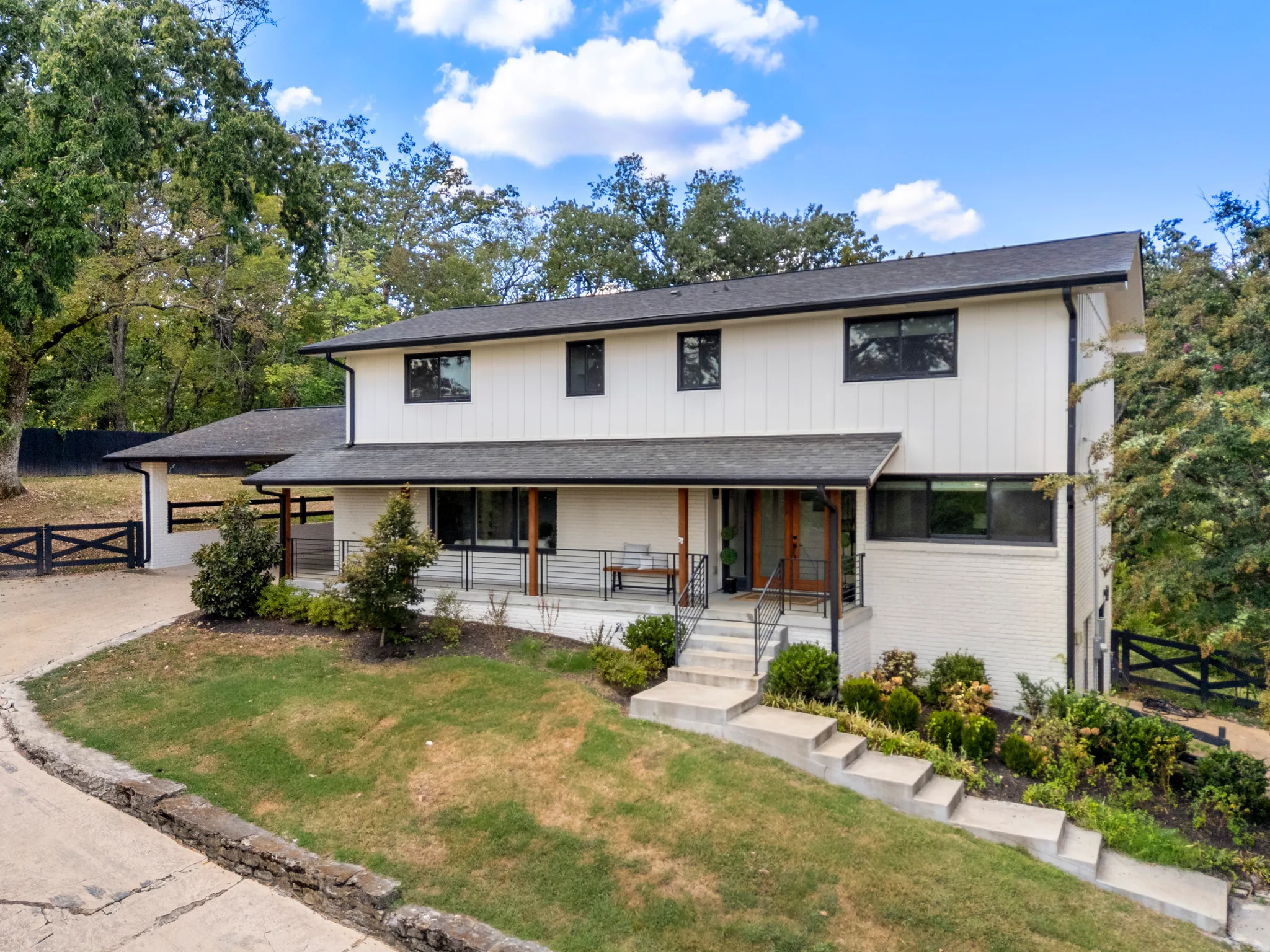 Two-story home with white board and batten upper level, painted brick lower level, covered front porch, and concrete steps rising through landscaped beds