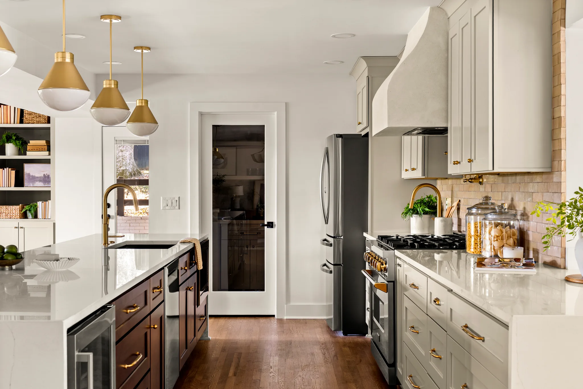 Kitchen with white quartz counters, dark wood island, plaster range hood, gold pendant lights and a glass-panel pantry door on oak floors