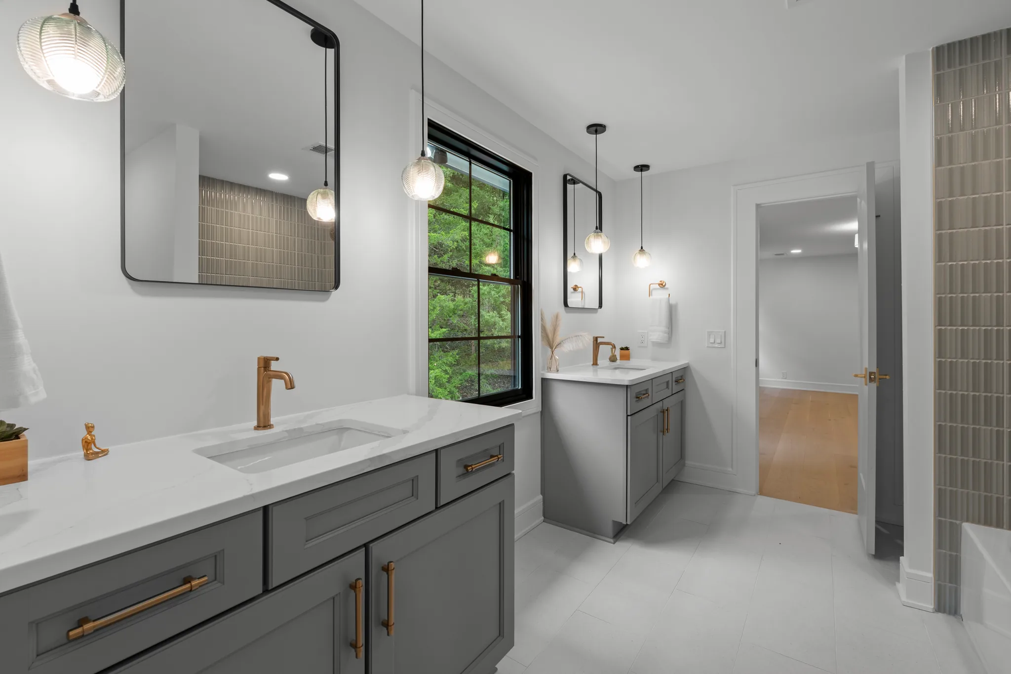 Bathroom with two separate gray shaker vanities, white quartz counters, brass faucets and hardware, black-framed mirrors and glass pendant lights