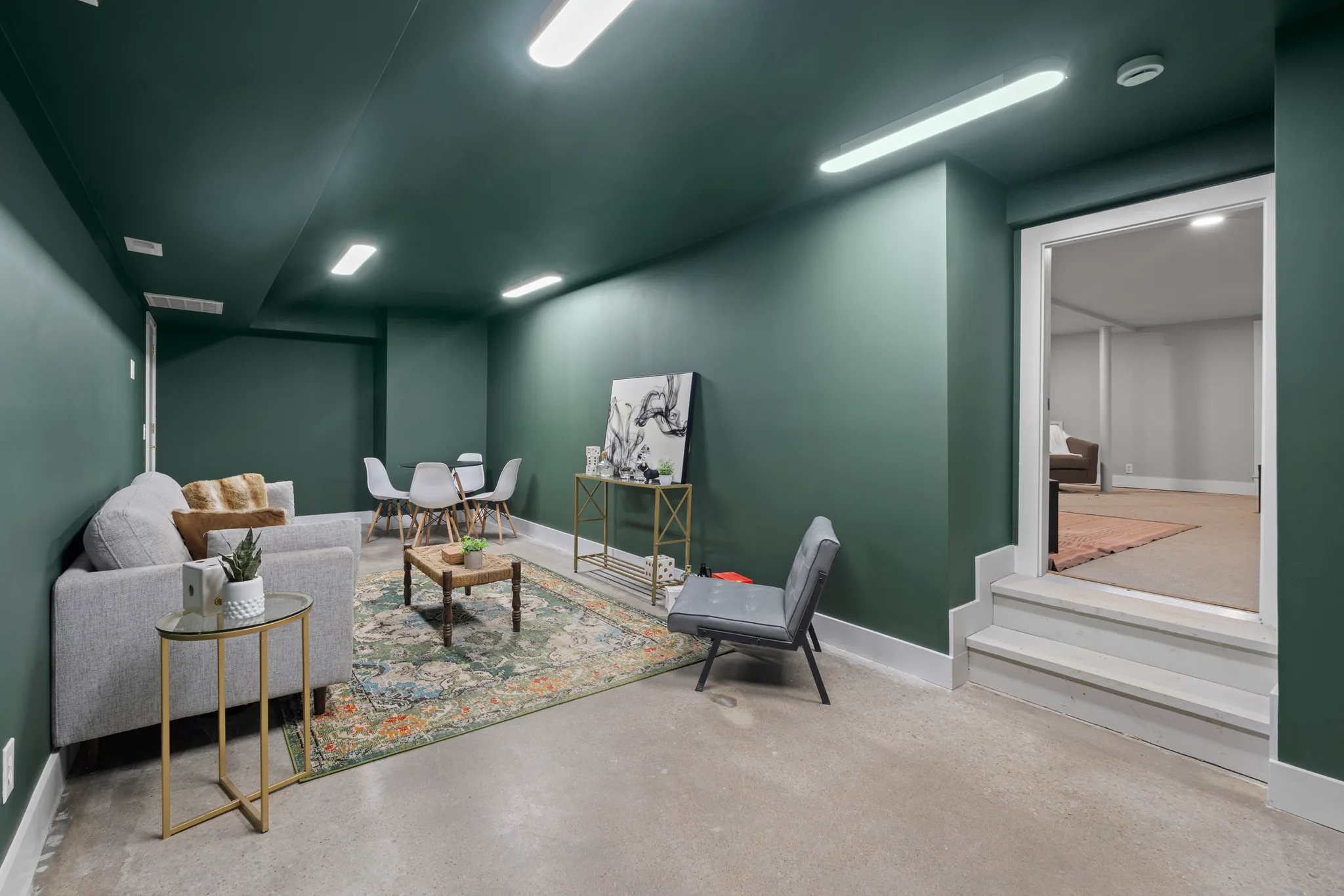 Finished basement sitting room with dark green walls and ceiling, polished concrete floor, patterned rug, and steps leading up to an adjoining room