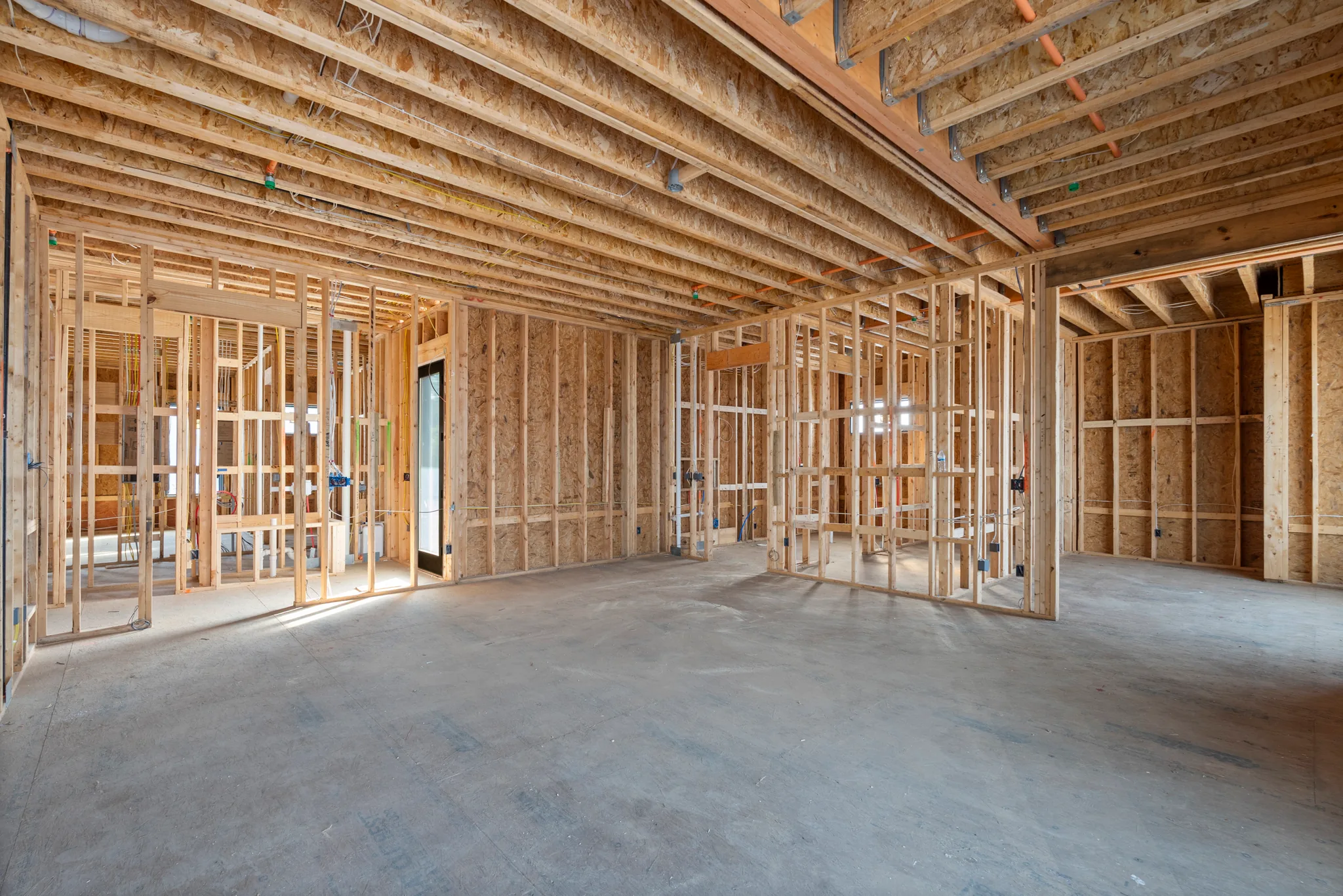 Interior wood stud framing under construction with exposed joists, electrical rough-in and a concrete slab floor lit by window openings