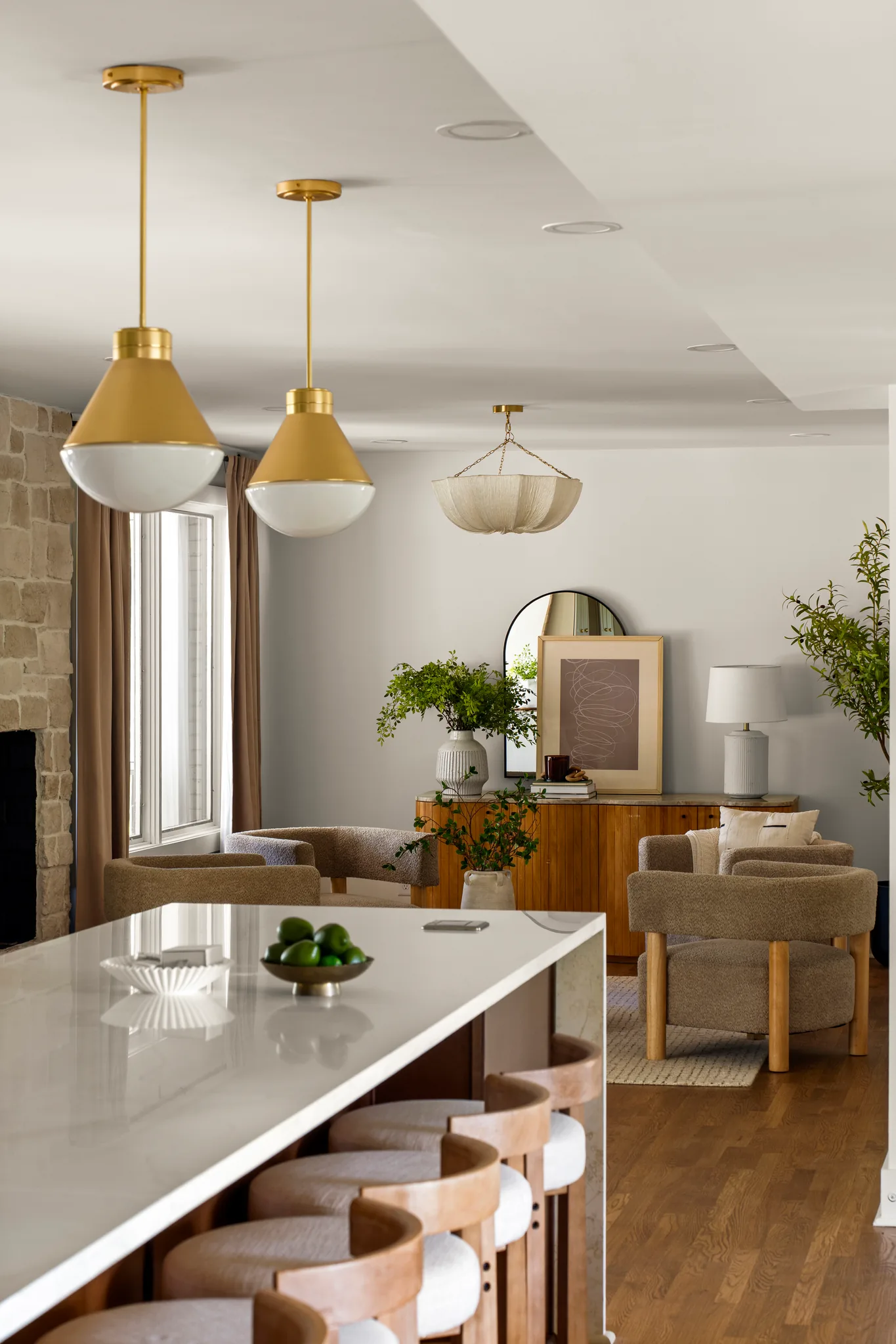 Kitchen island with white quartz waterfall counter, wood stools and two brass pendants, opening to a sitting area with oak floors