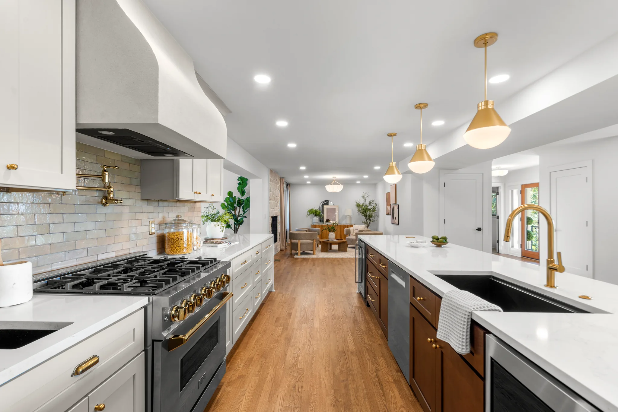 Kitchen with white perimeter cabinets, plaster hood, glazed tile backsplash and walnut island with brass pendants, looking toward a living area