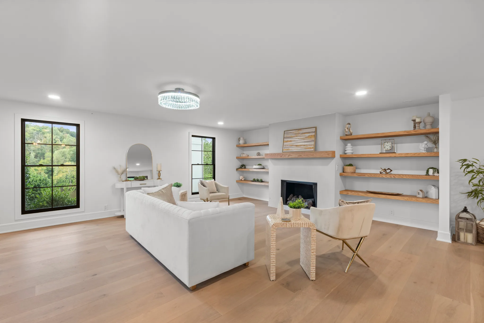 Open living room with a white plaster fireplace, stained wood floating shelves, black grid windows and wide light oak plank flooring