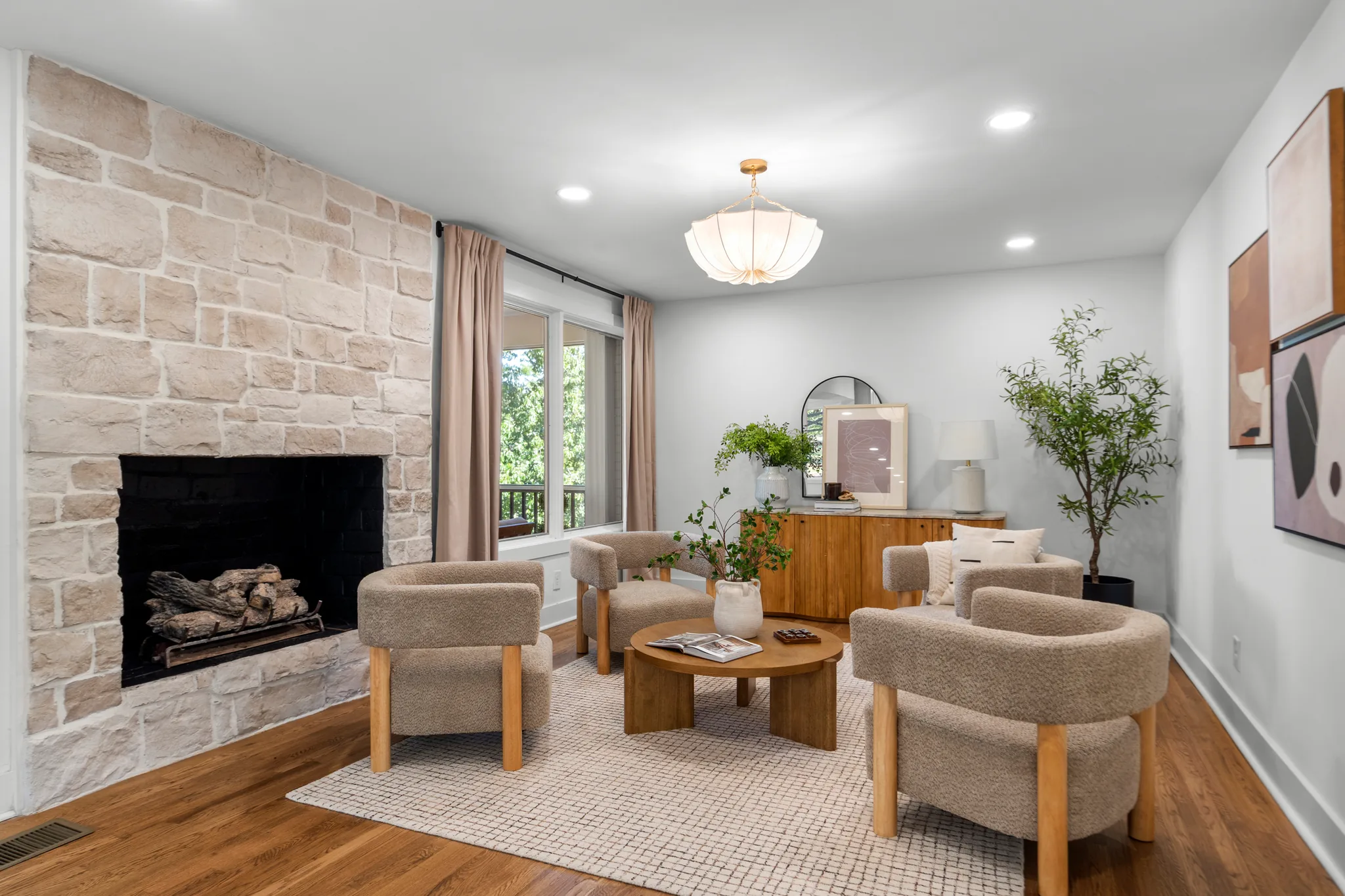 Living room with a light stone fireplace wall, black firebox, hardwood floors, four boucle armchairs and a round wood coffee table