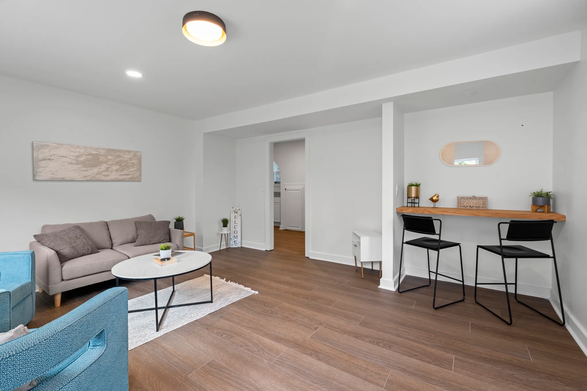 Renovated sitting room with white walls, wood-look plank flooring, a gray sofa, teal armchairs and a wood counter with two black stools