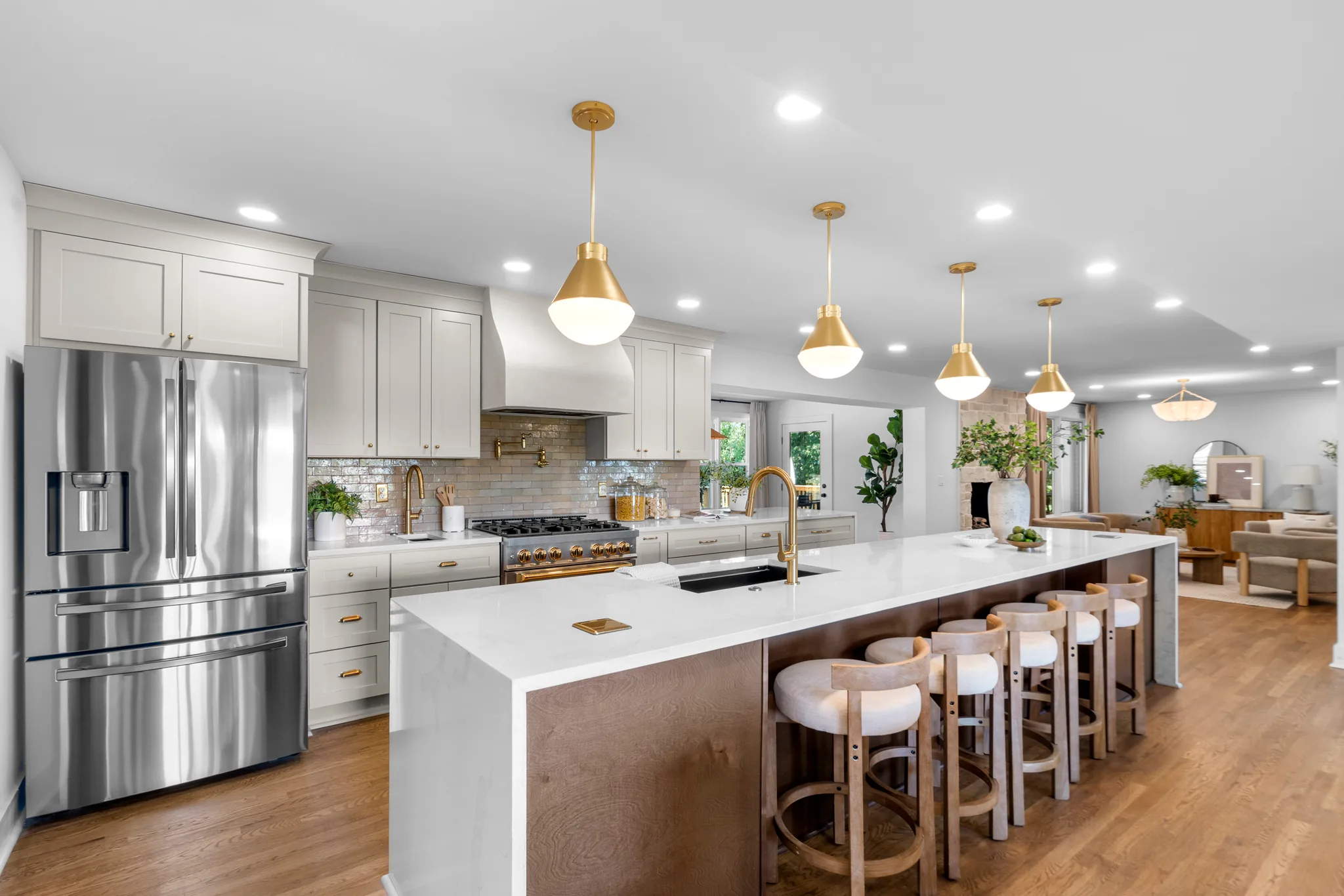 Kitchen with white cabinets, plaster range hood, brass pendants and a long white quartz island with wood base and upholstered stools