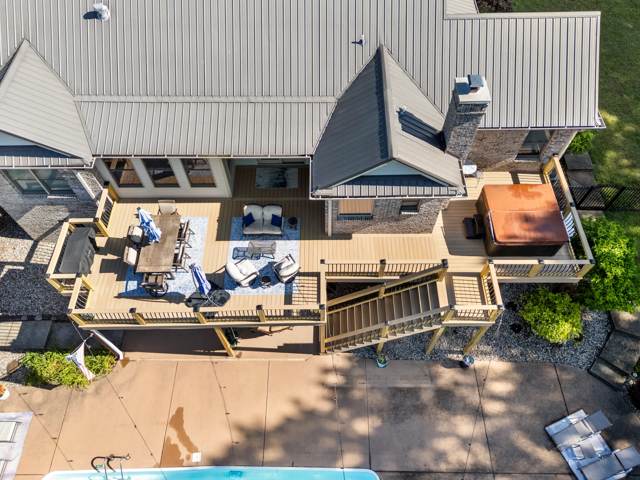 Aerial view of a composite deck with dining table, lounge chairs, hot tub and stairs beside a covered porch under a metal roof