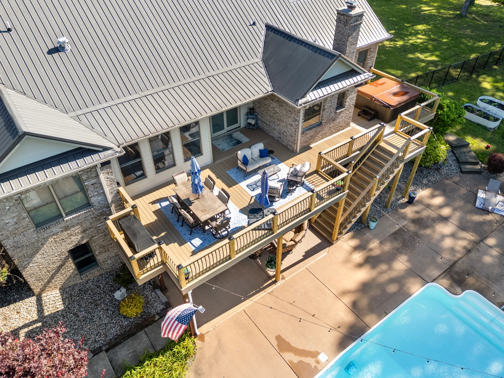 Aerial view of a raised composite deck with wood posts and black balusters beside a brick home with a standing seam metal roof and pool patio