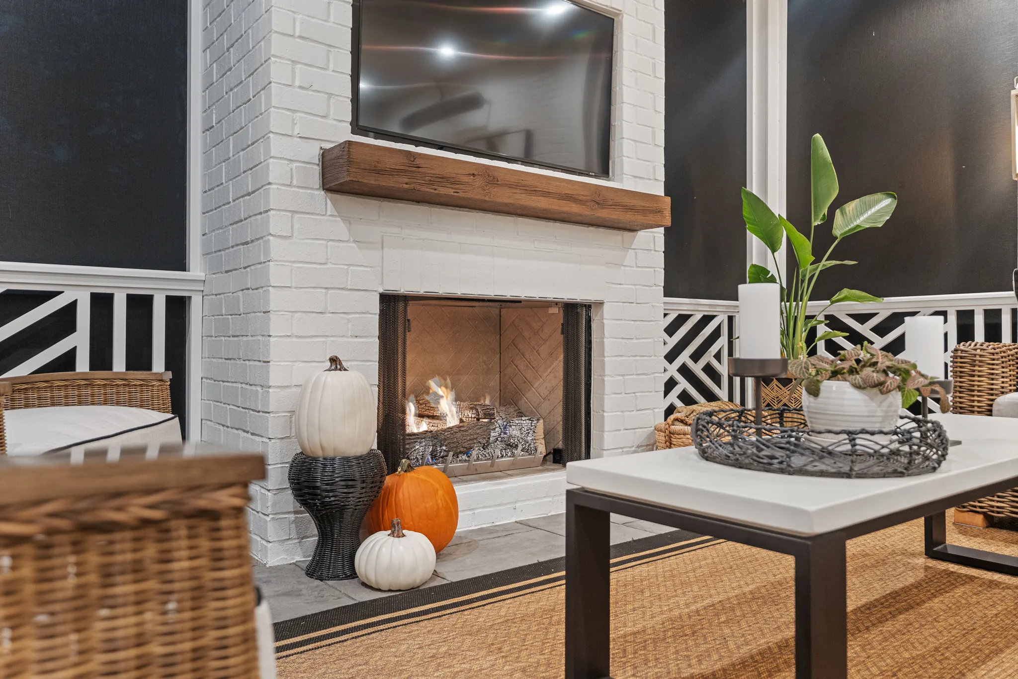 Painted white brick fireplace with a thick stained wood mantel and mounted TV on a porch with dark walls and white Chippendale railing
