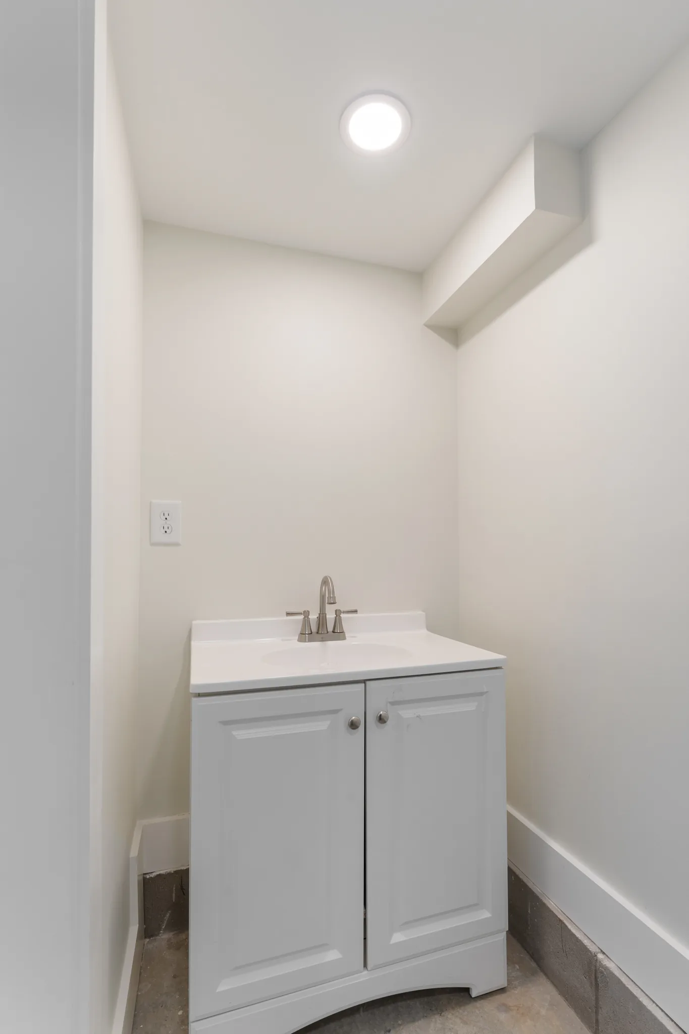 Compact powder room with a white two-door vanity, integrated white sink, brushed nickel faucet, pale walls and a round ceiling light