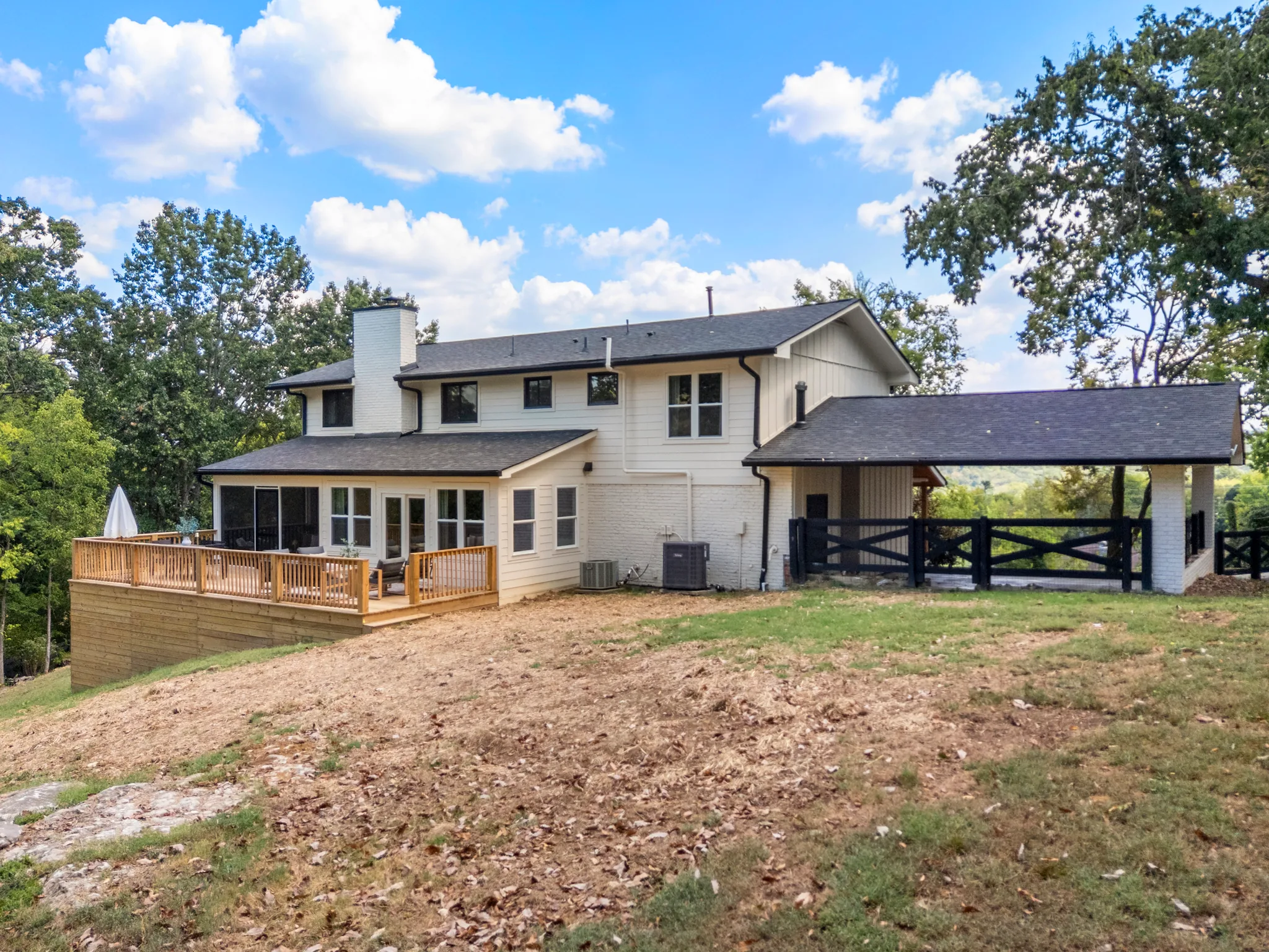 Rear of a white two-story house with screened porch, wood deck, painted brick chimney and an attached carport with black rail fencing