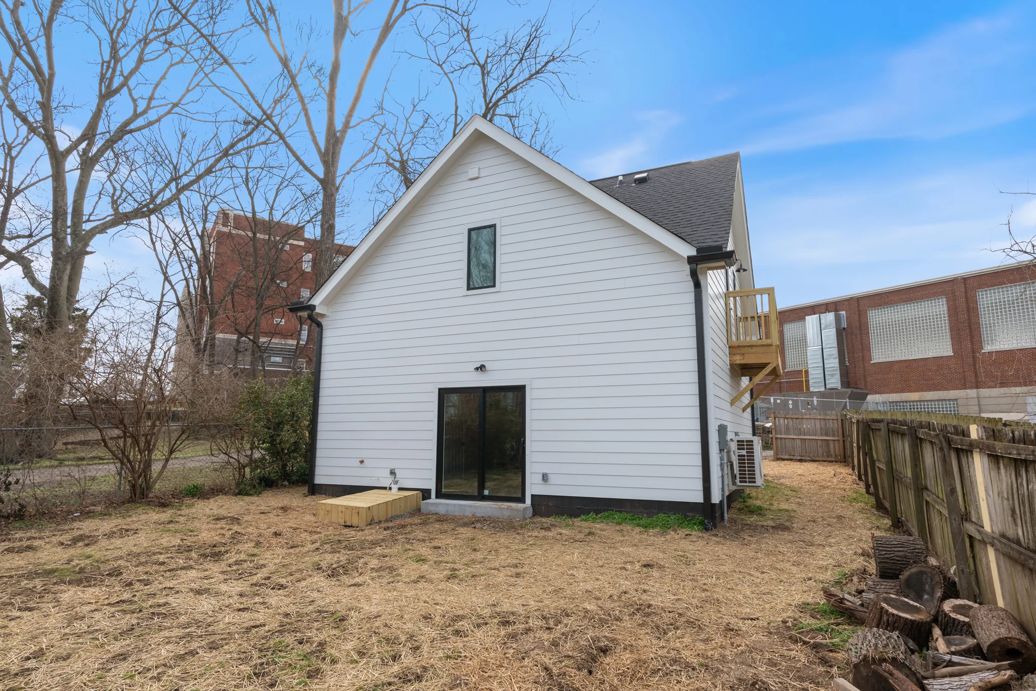Rear elevation of a white lap-sided two-story home with a black-framed glass door, small wood landing, side balcony and wood privacy fence