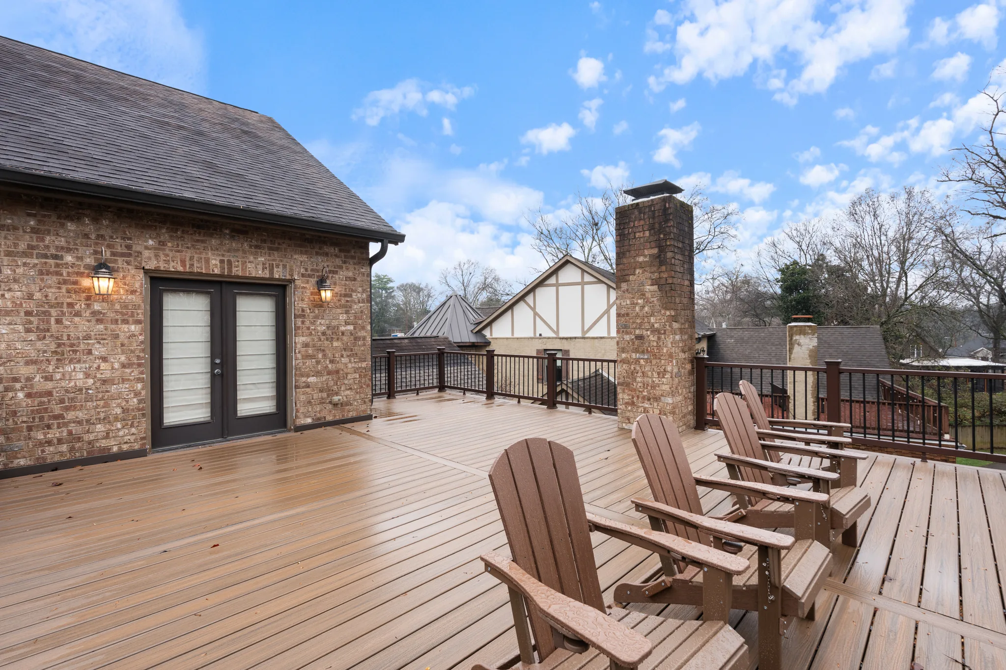 Large composite deck beside a brick home with French doors, black metal railing, brick chimney and four brown Adirondack chairs