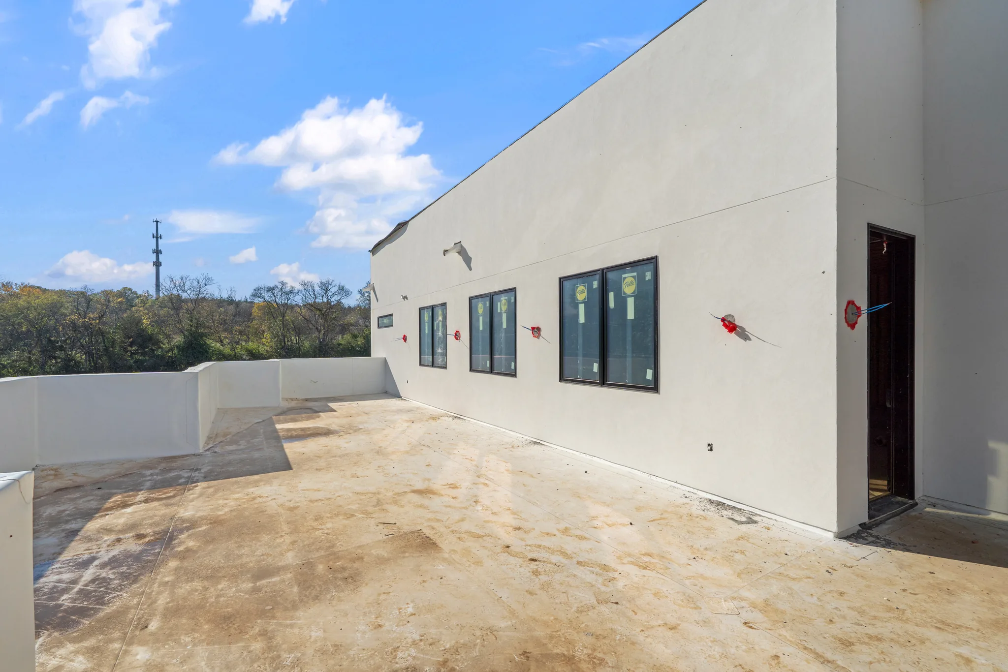 Flat rooftop terrace under construction with white stucco parapet walls, labeled storefront windows, open doorway and exposed concrete deck