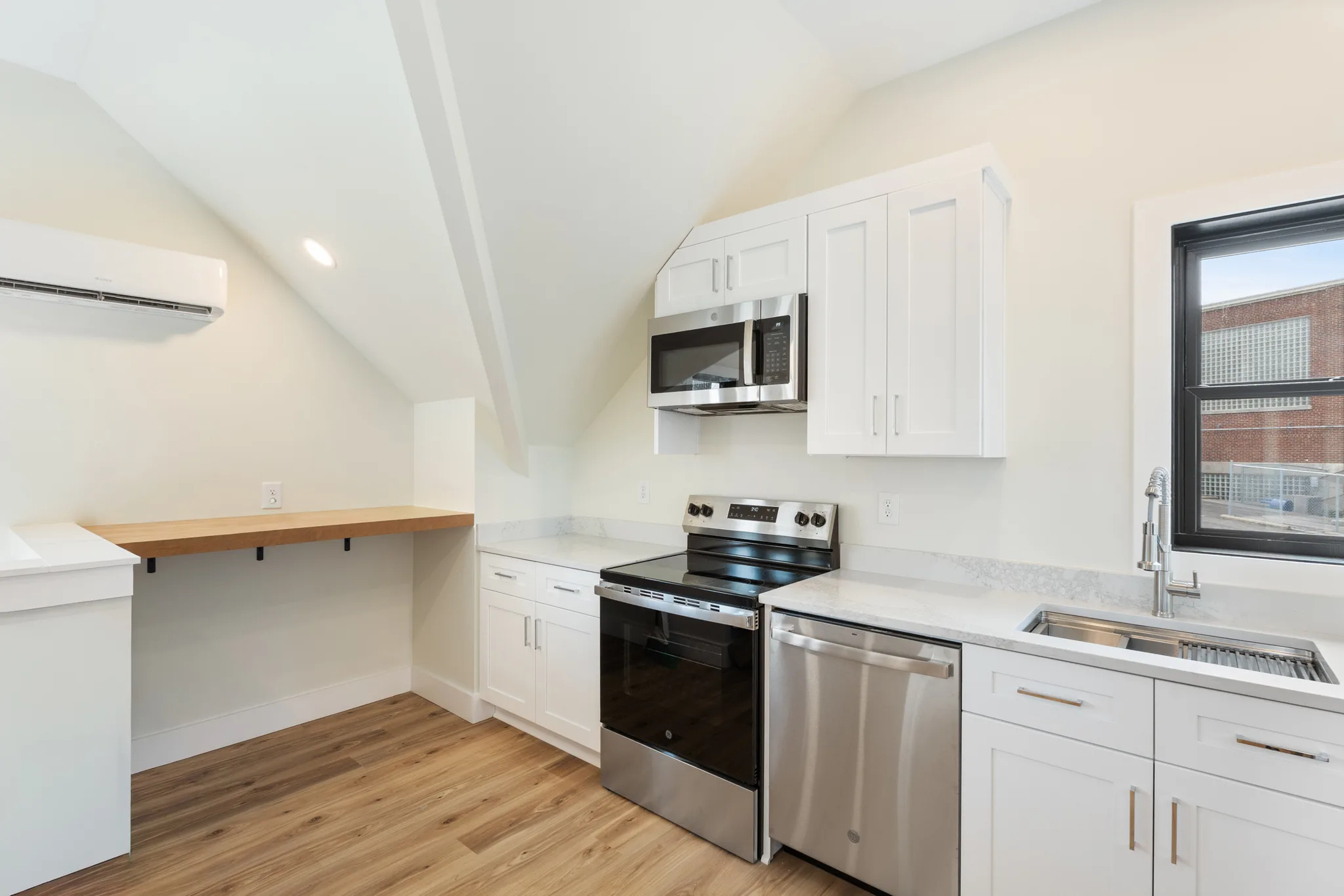 Compact kitchen with white shaker cabinets, quartz counters, stainless range and dishwasher, sloped ceiling, wall mini-split and butcher block wall ledge
