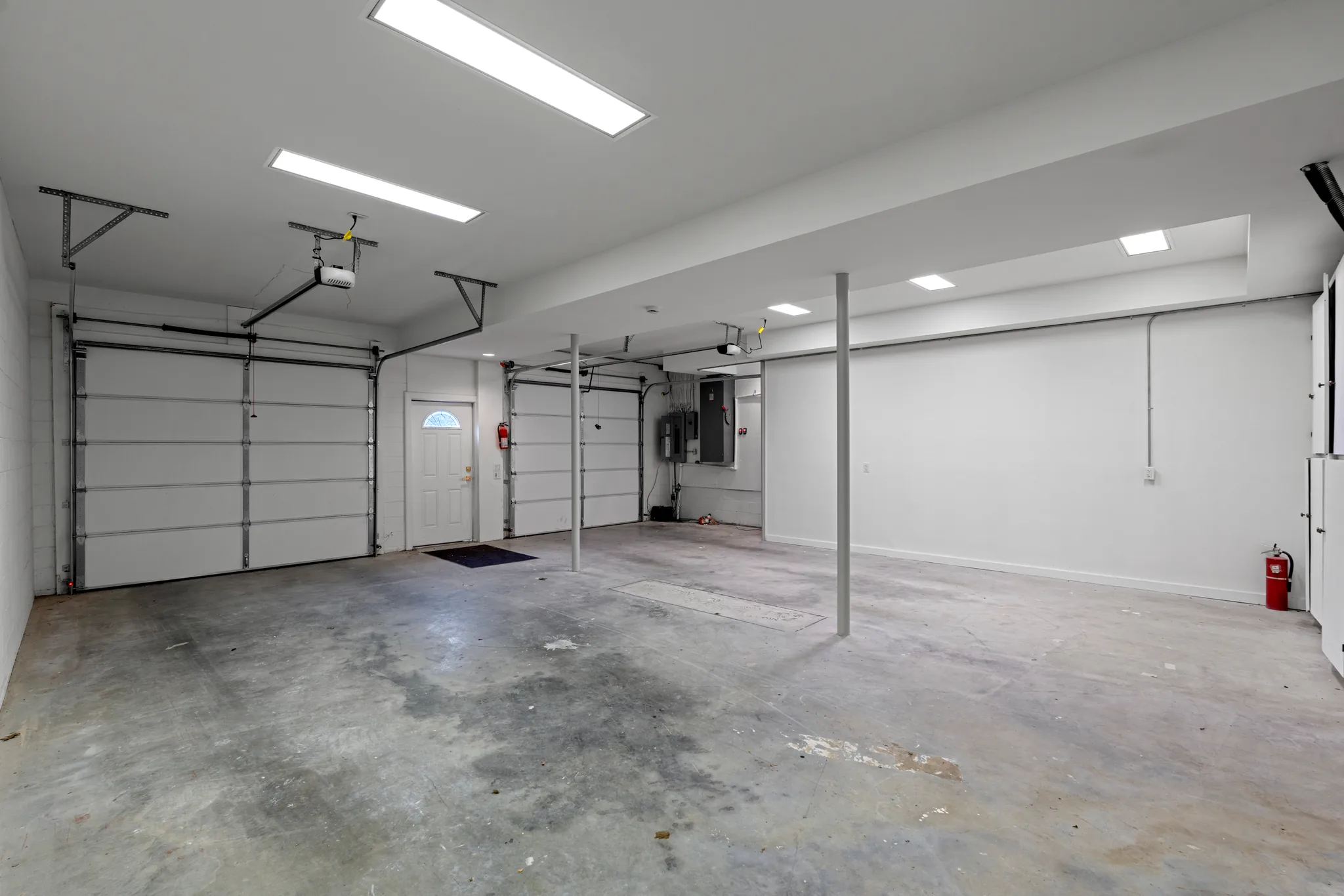 Interior of a finished three-bay garage with white walls, sectional overhead doors, steel support columns and a sealed concrete floor