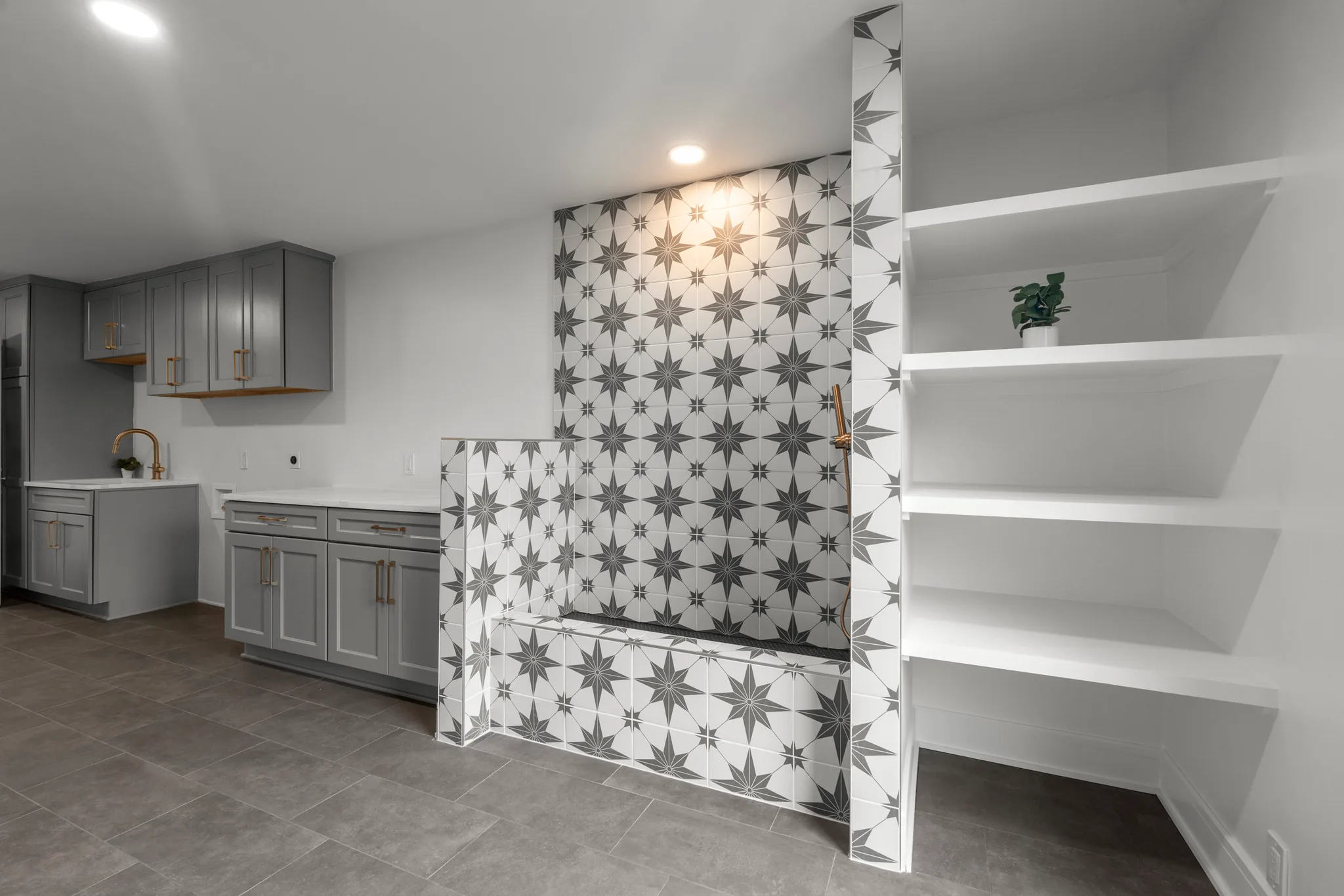 Basement room with a star-patterned black and white tile alcove and bench, gray cabinets with brass hardware, and white built-in shelving