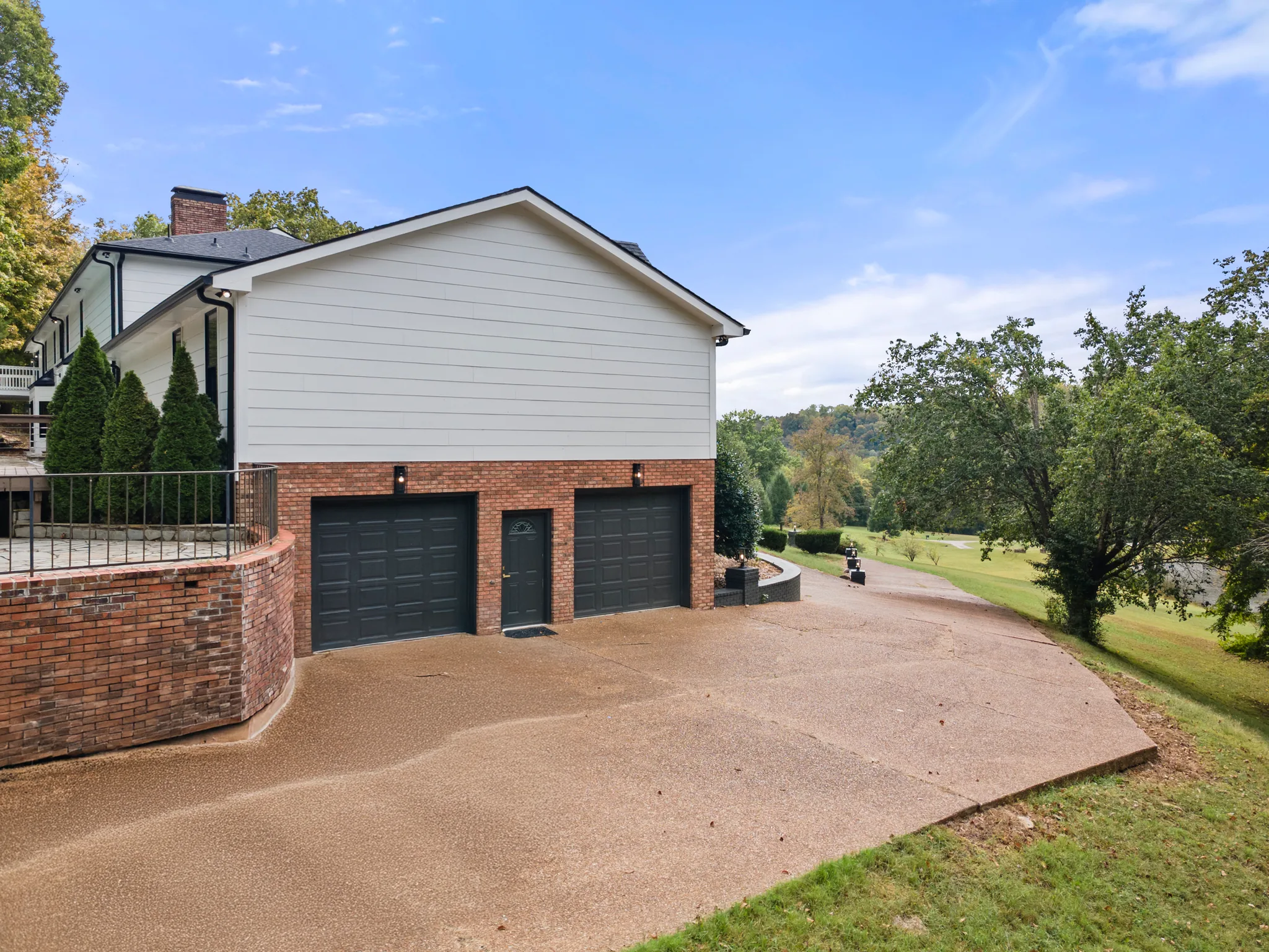 Side view of a two-car garage with brick lower walls, dark garage doors and white lap siding above, fronted by a wide concrete driveway