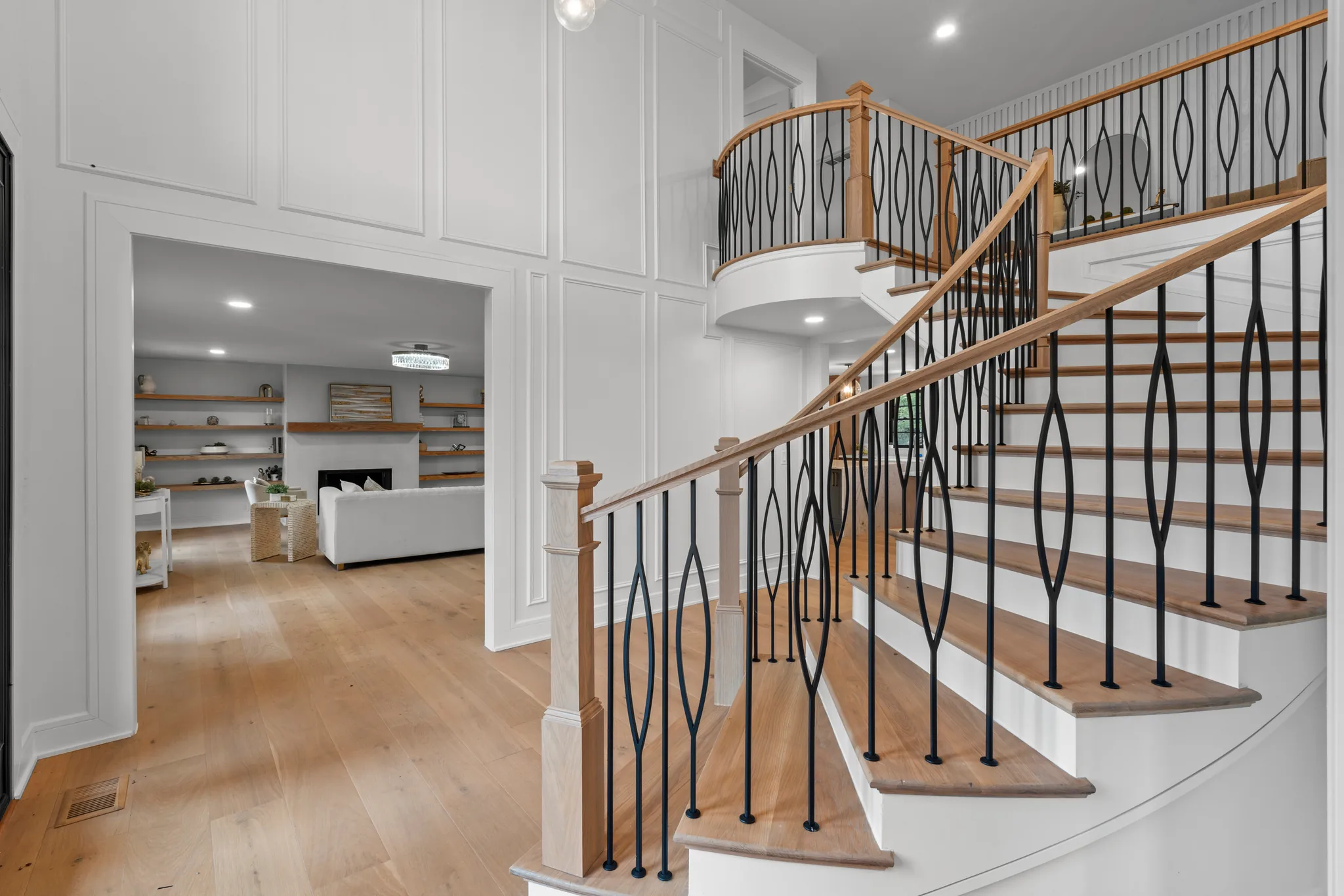 Two-story entry with a curving staircase, oak treads, black metal balusters and a wood handrail beside white paneled walls and wide oak floors