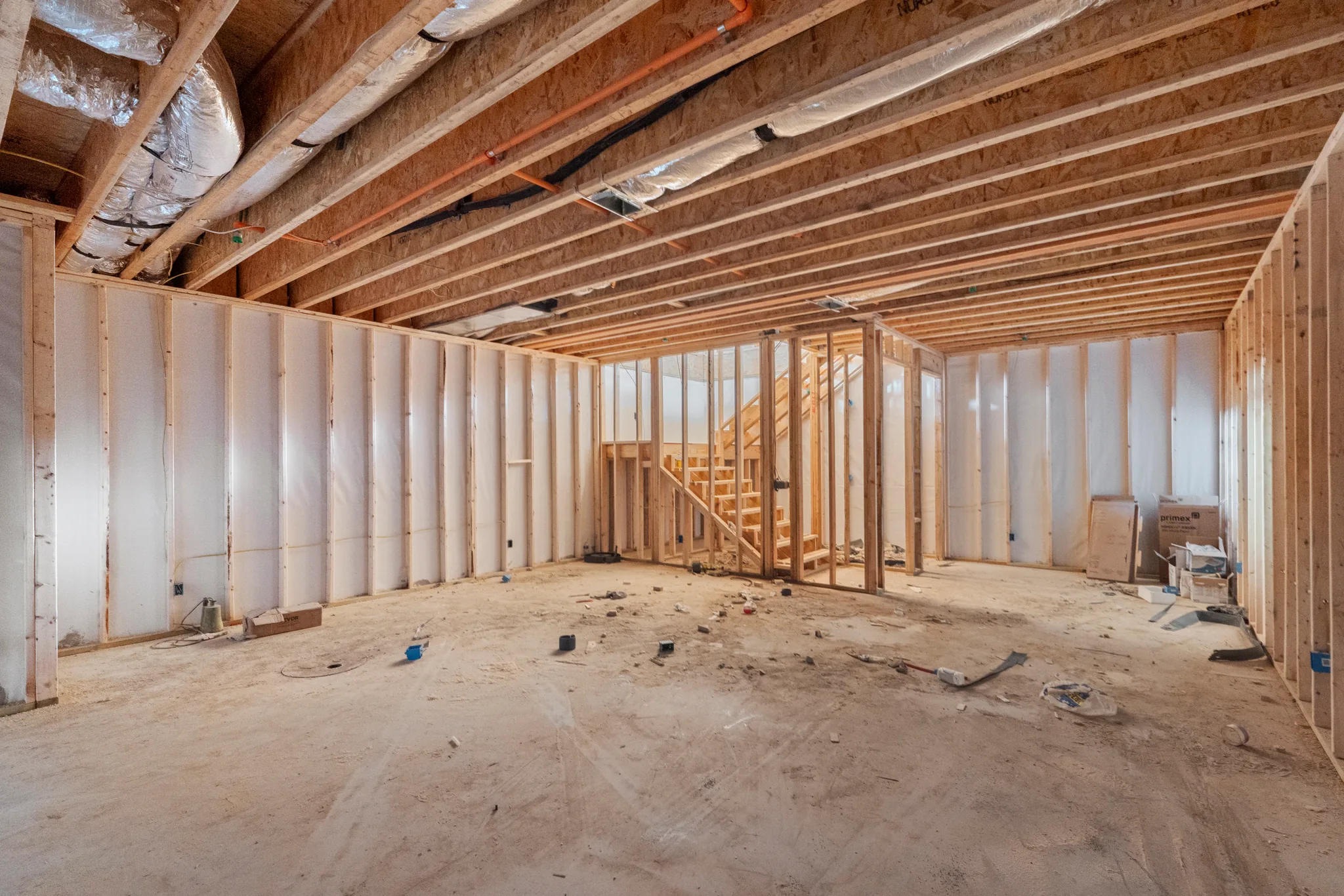 Unfinished basement under construction with framed stud walls, white insulation wrap, exposed floor joists, ductwork and wiring above a dirt floor